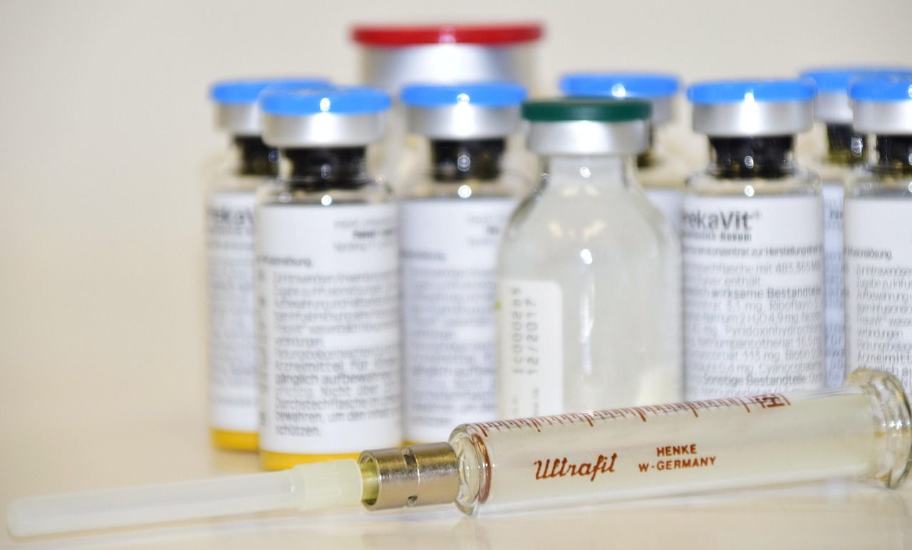 Glass medicine vials with blue caps and an old glass syringe on a white table