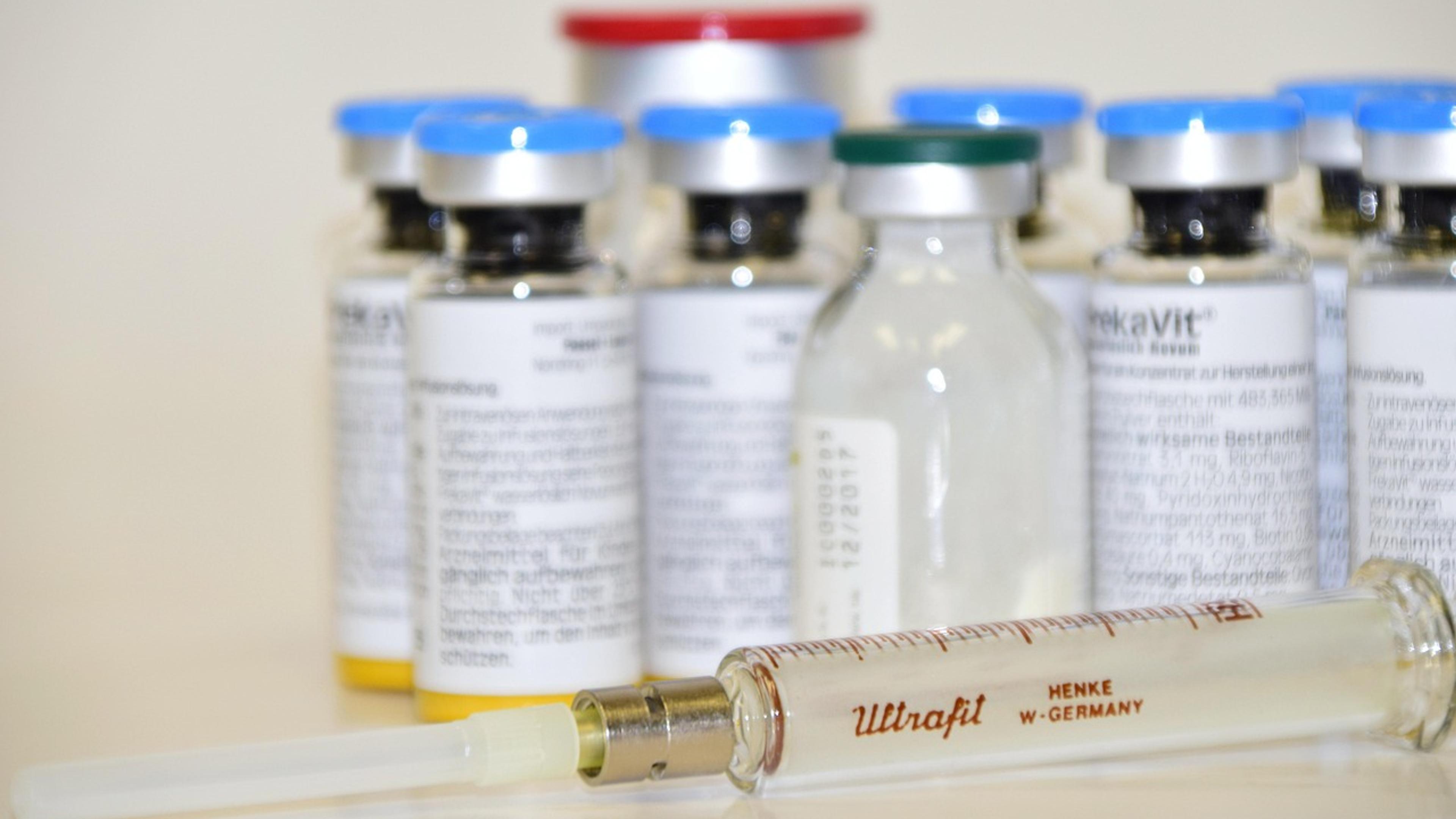 Glass medicine vials with blue caps and an old glass syringe on a white table