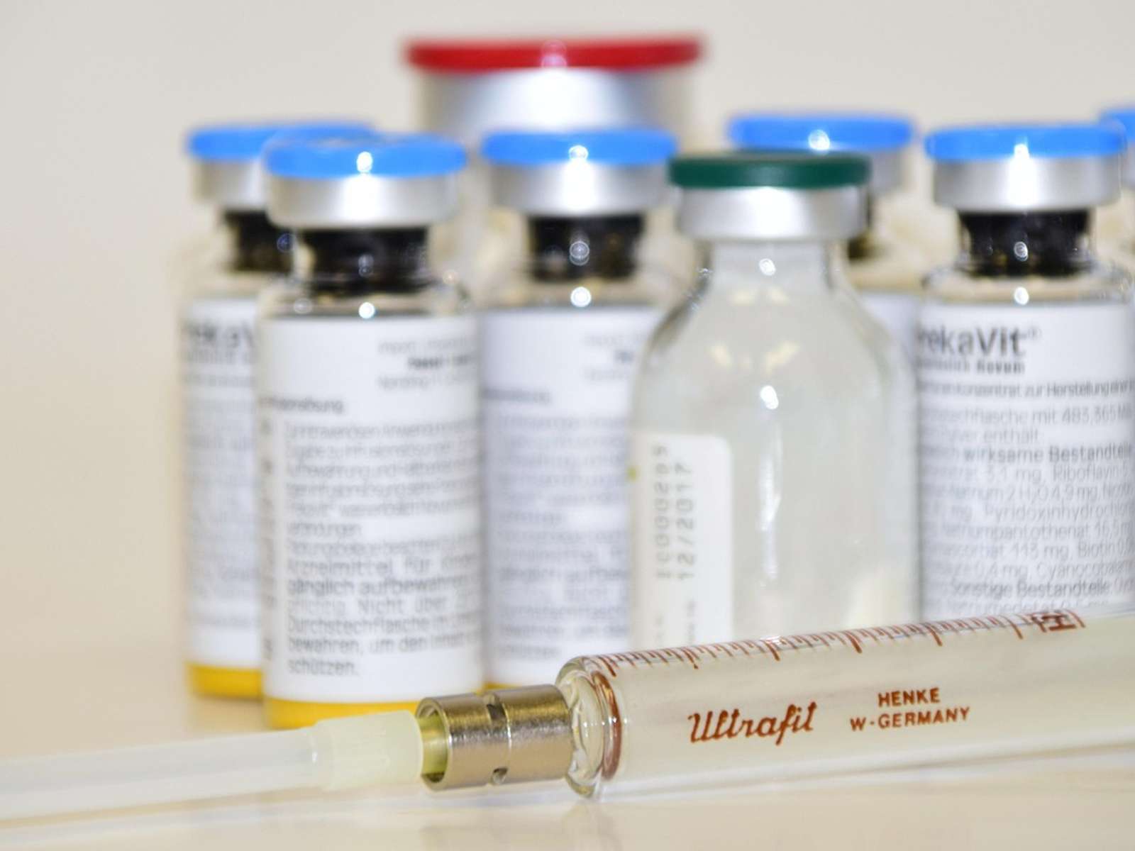Glass medicine vials with blue caps and an old glass syringe on a white table