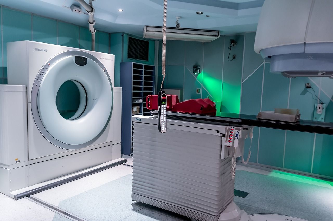 A hospital treatment room with a ring-shaped scanner and a patient table under green-tinted lighting