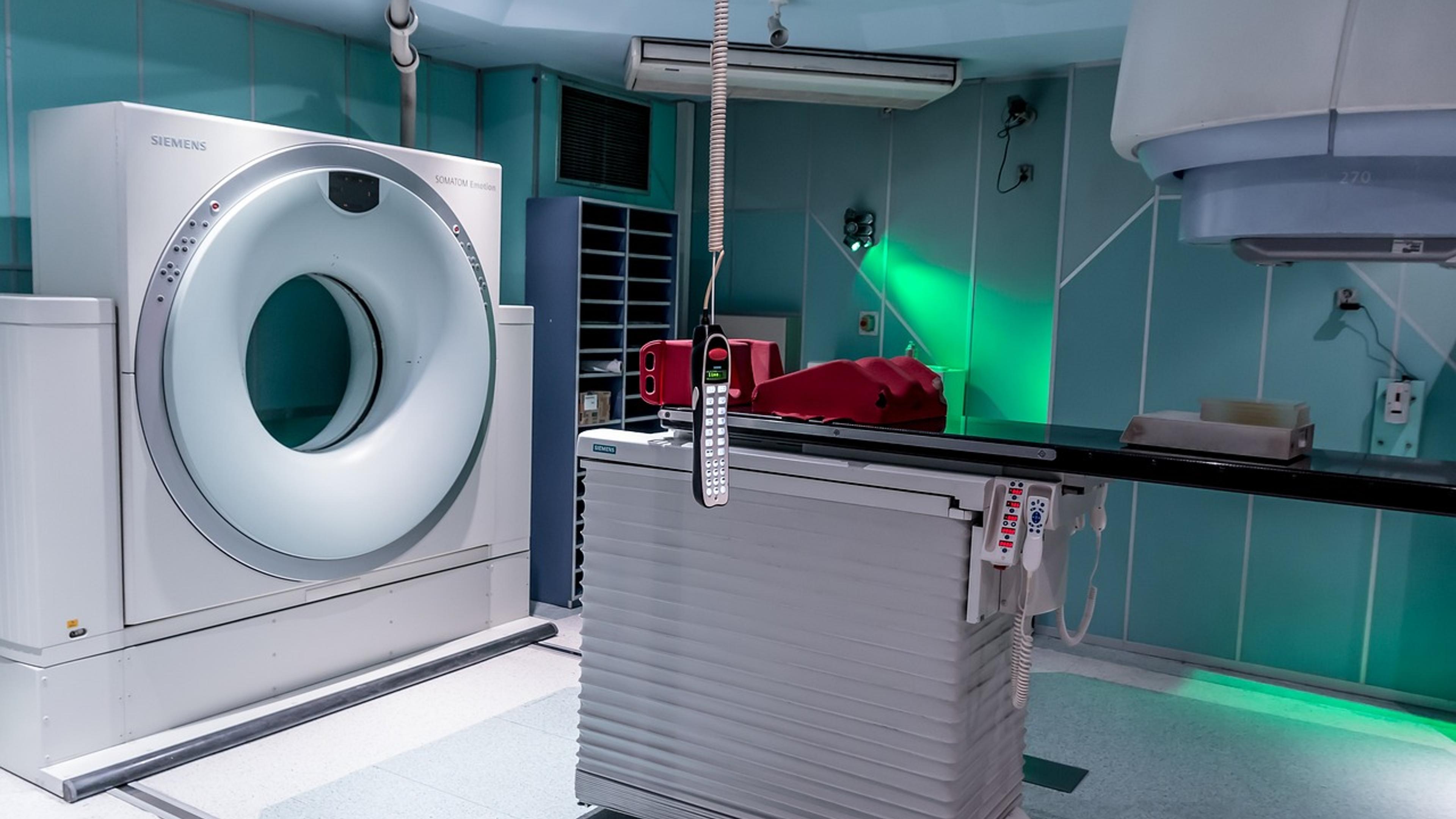 A hospital treatment room with a ring-shaped scanner and a patient table under green-tinted lighting