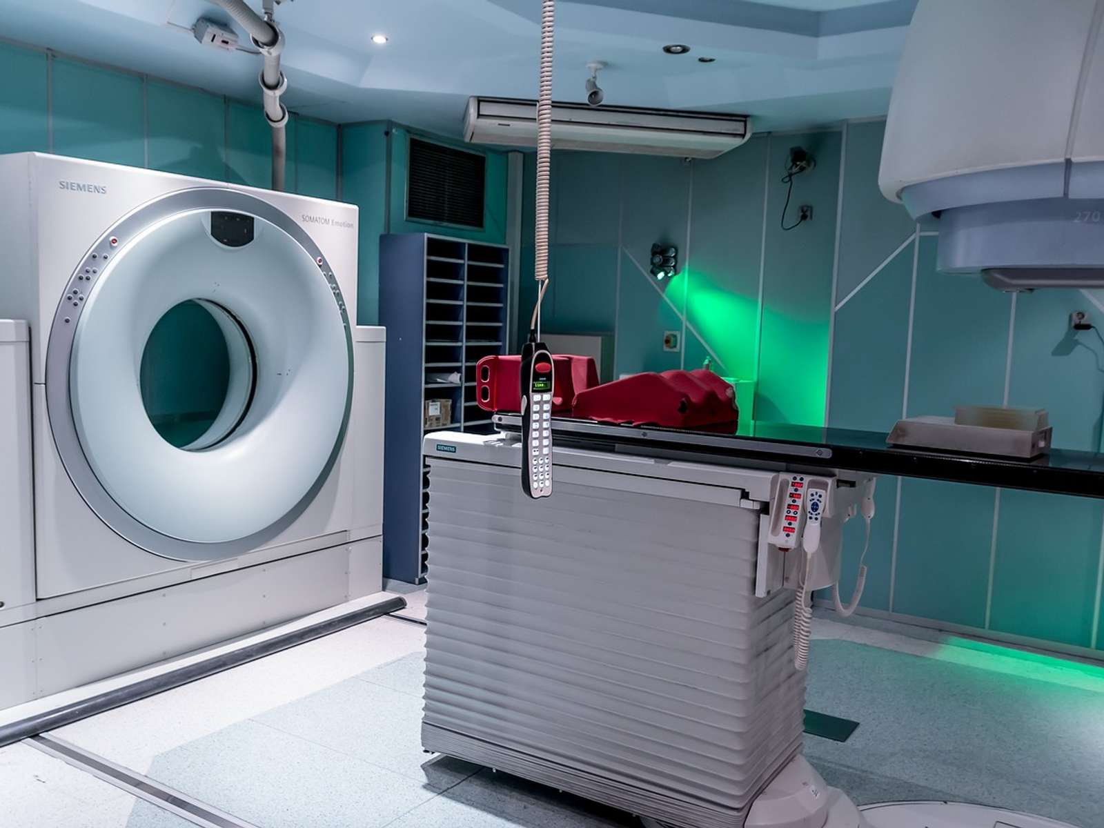 A hospital treatment room with a ring-shaped scanner and a patient table under green-tinted lighting