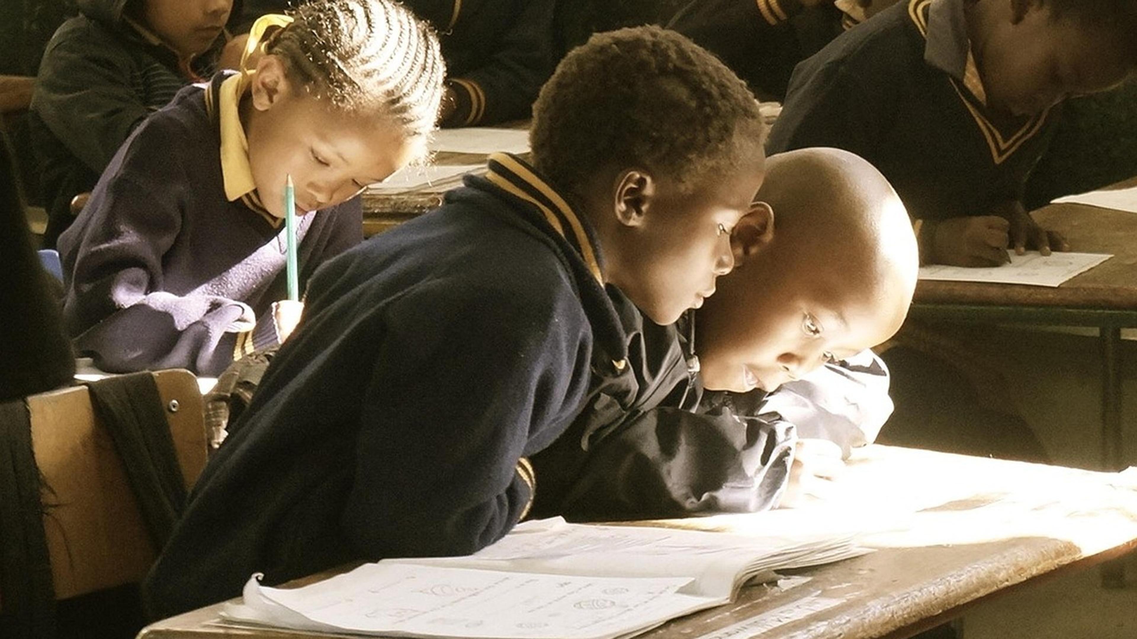 Students bent over their notebooks, writing at desks in a classroom