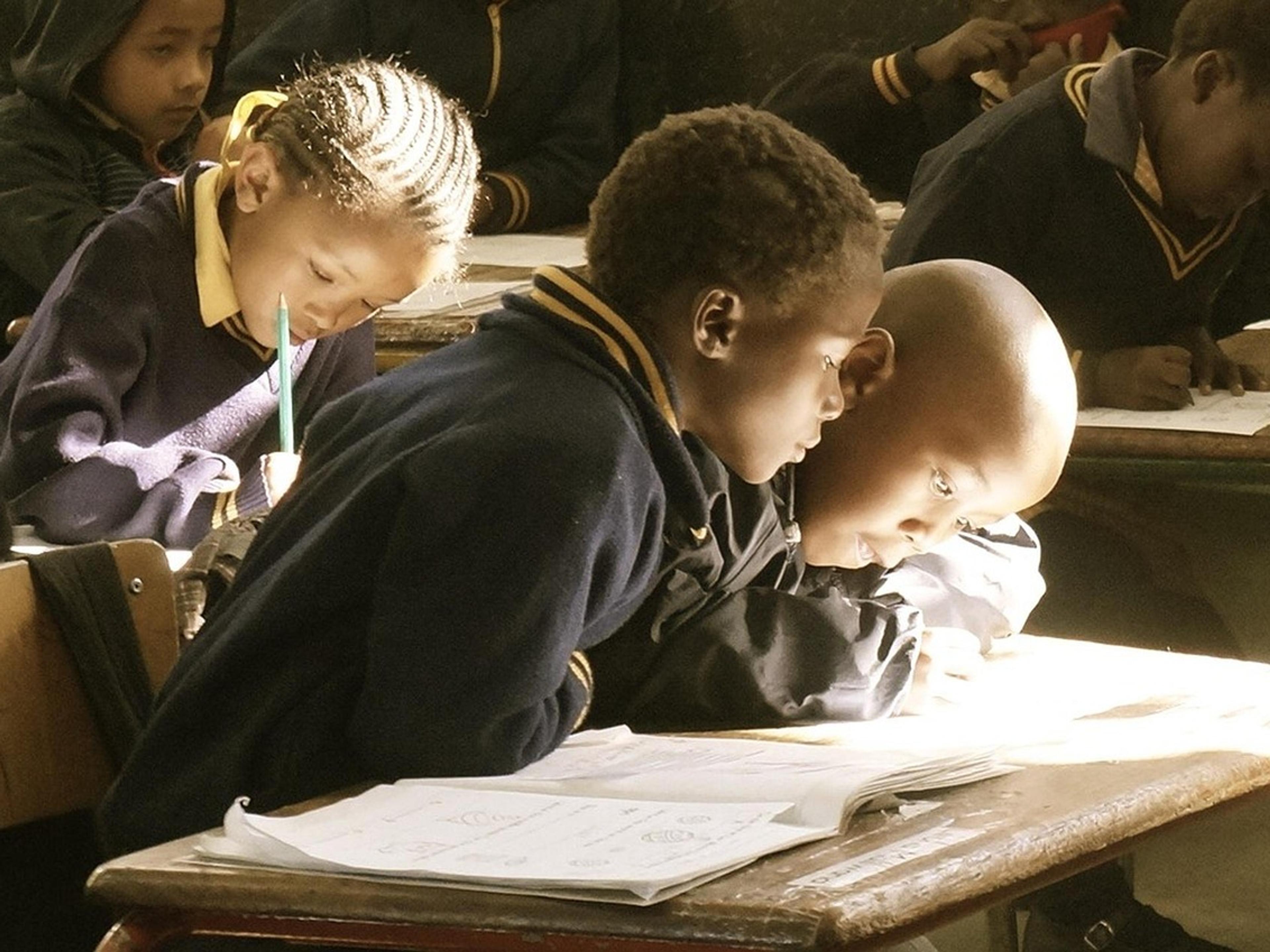 Students bent over their notebooks, writing at desks in a classroom