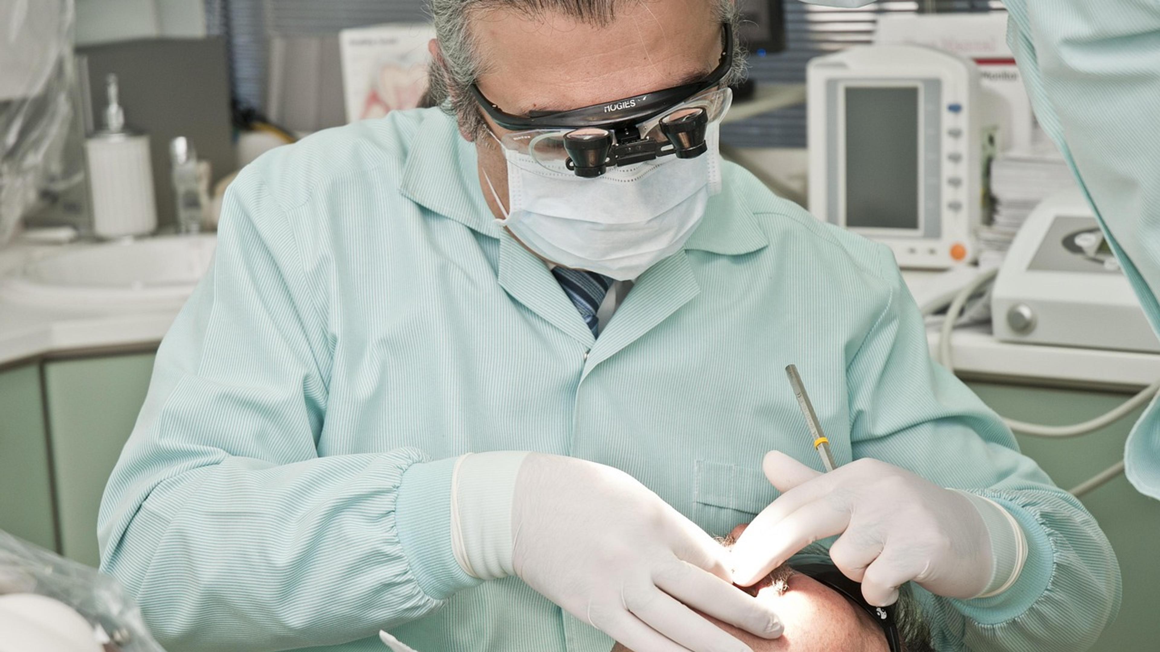 A dentist wearing magnifying loupes and gloves treating a patient
