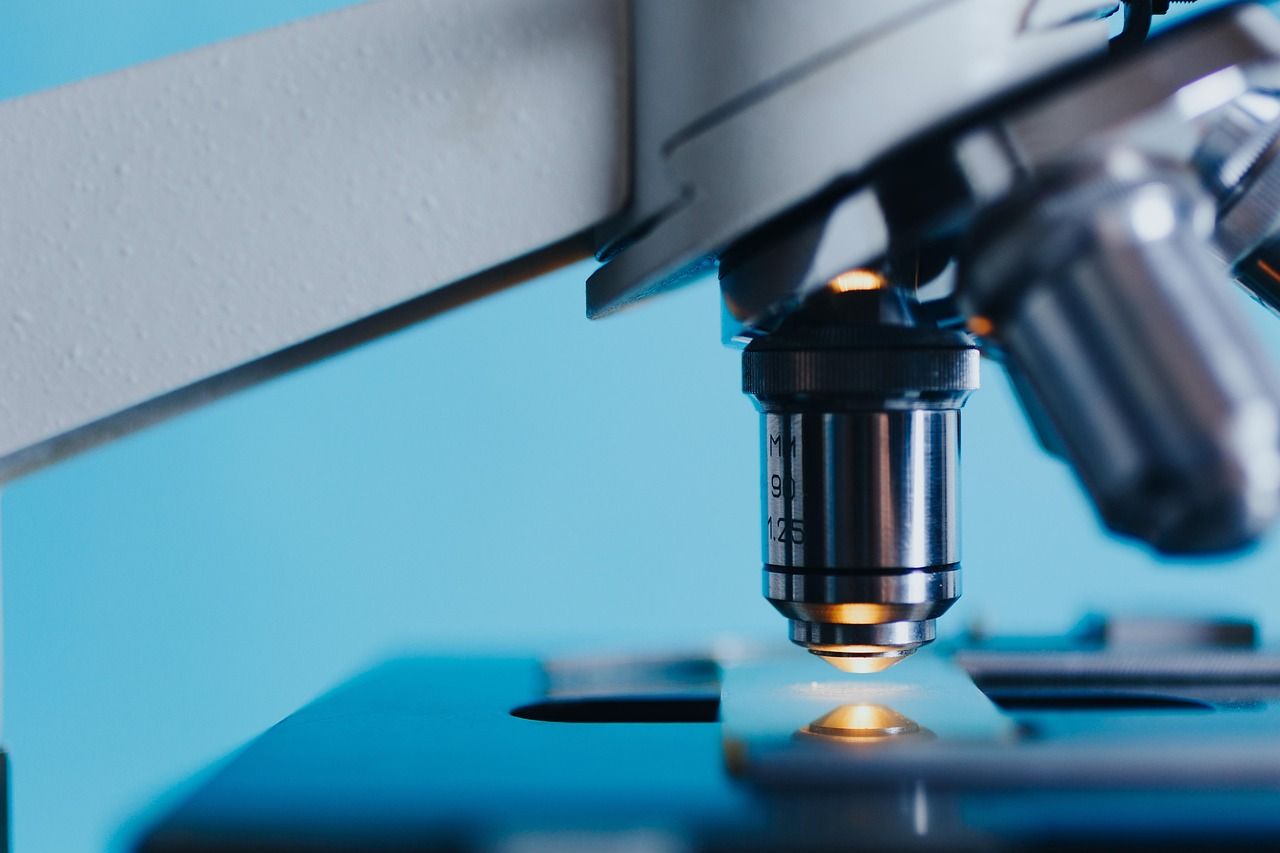 Close-up of a microscope objective lens above a glass slide in blue light