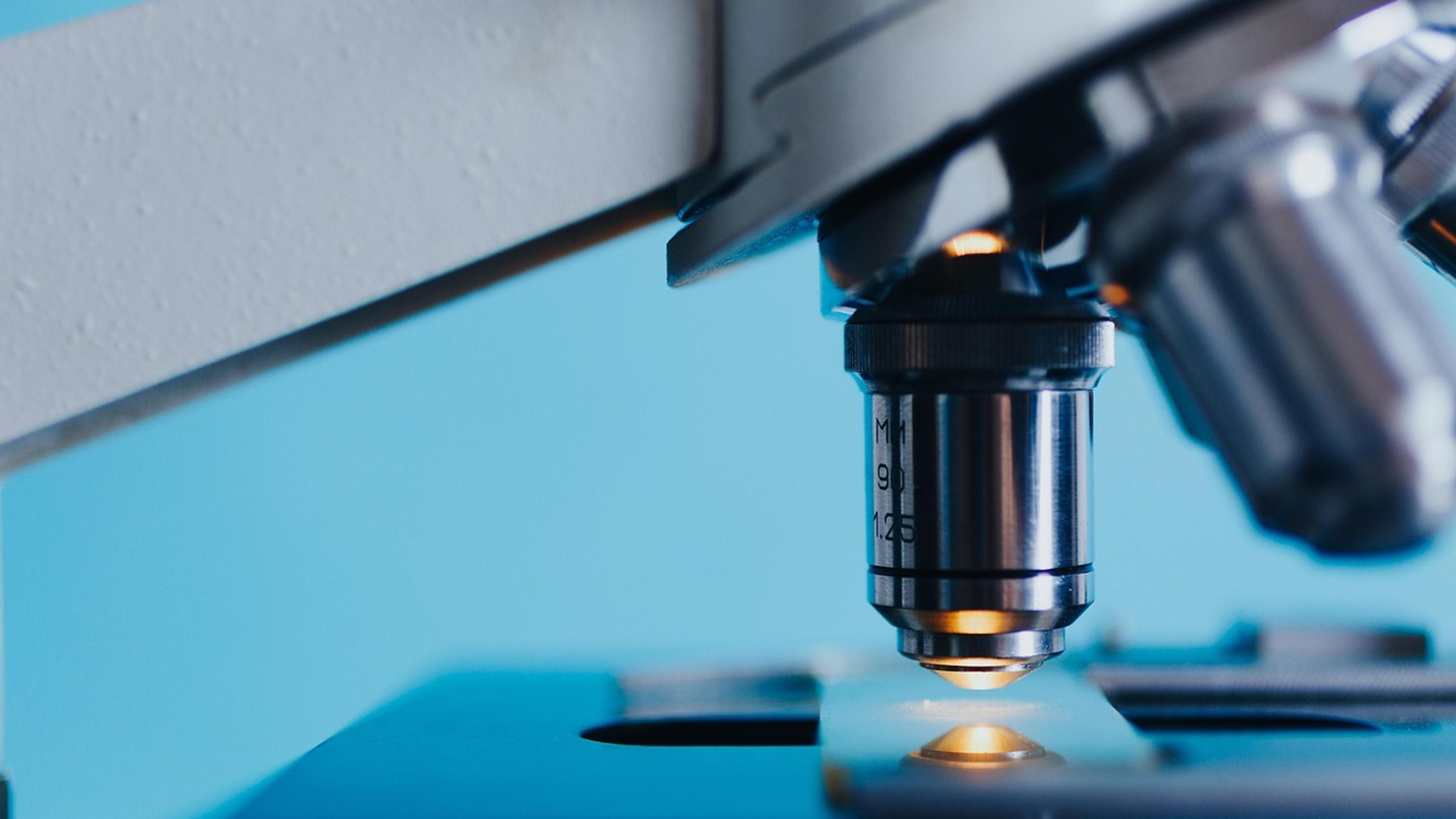 Close-up of a microscope objective lens above a glass slide in blue light