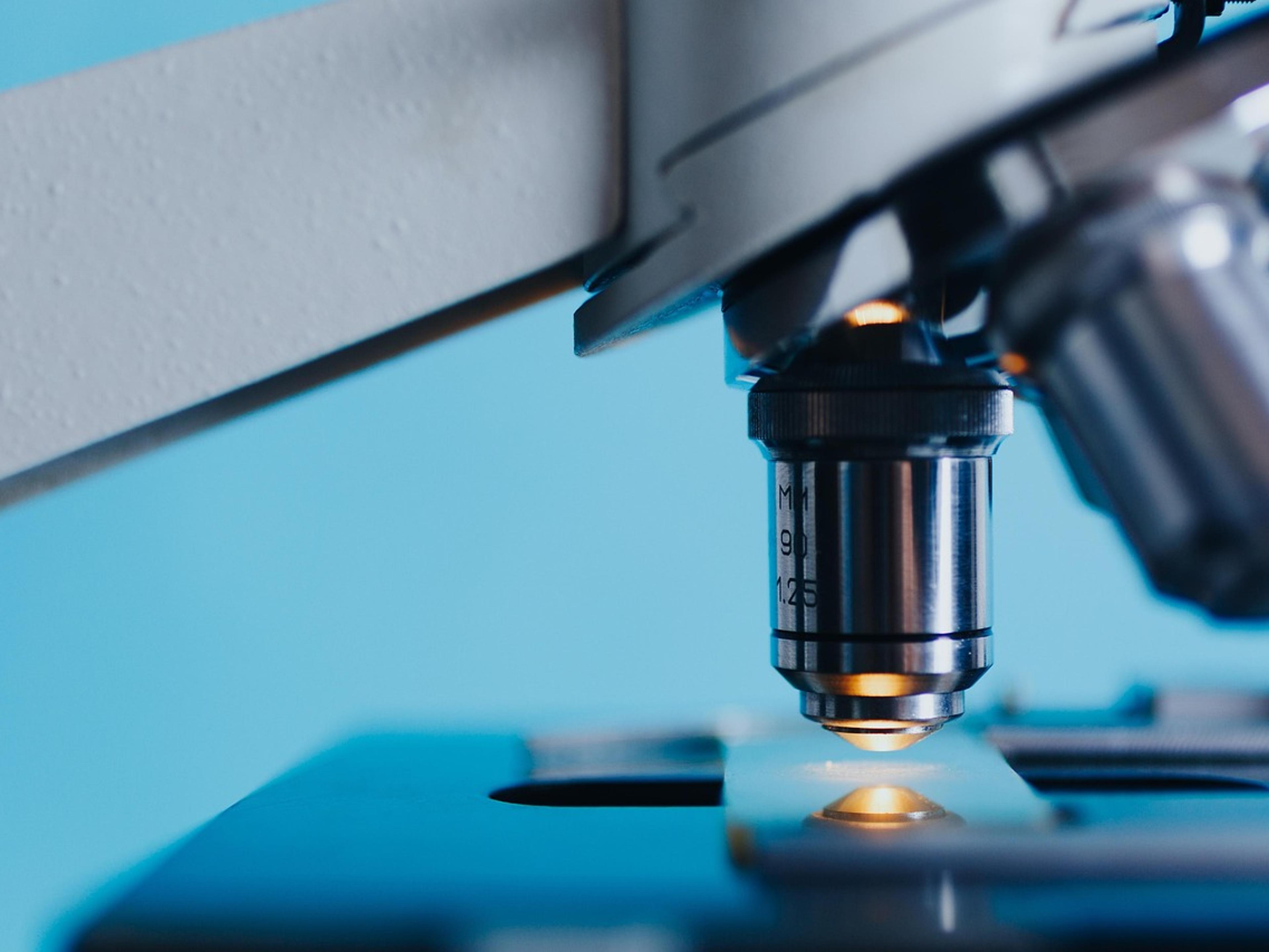 Close-up of a microscope objective lens above a glass slide in blue light