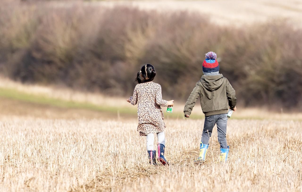 Two young children in boots and jackets running across a mown field