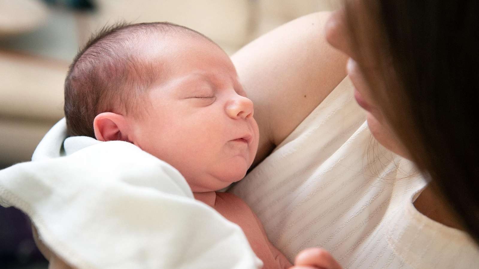 A sleeping newborn baby held by its mother