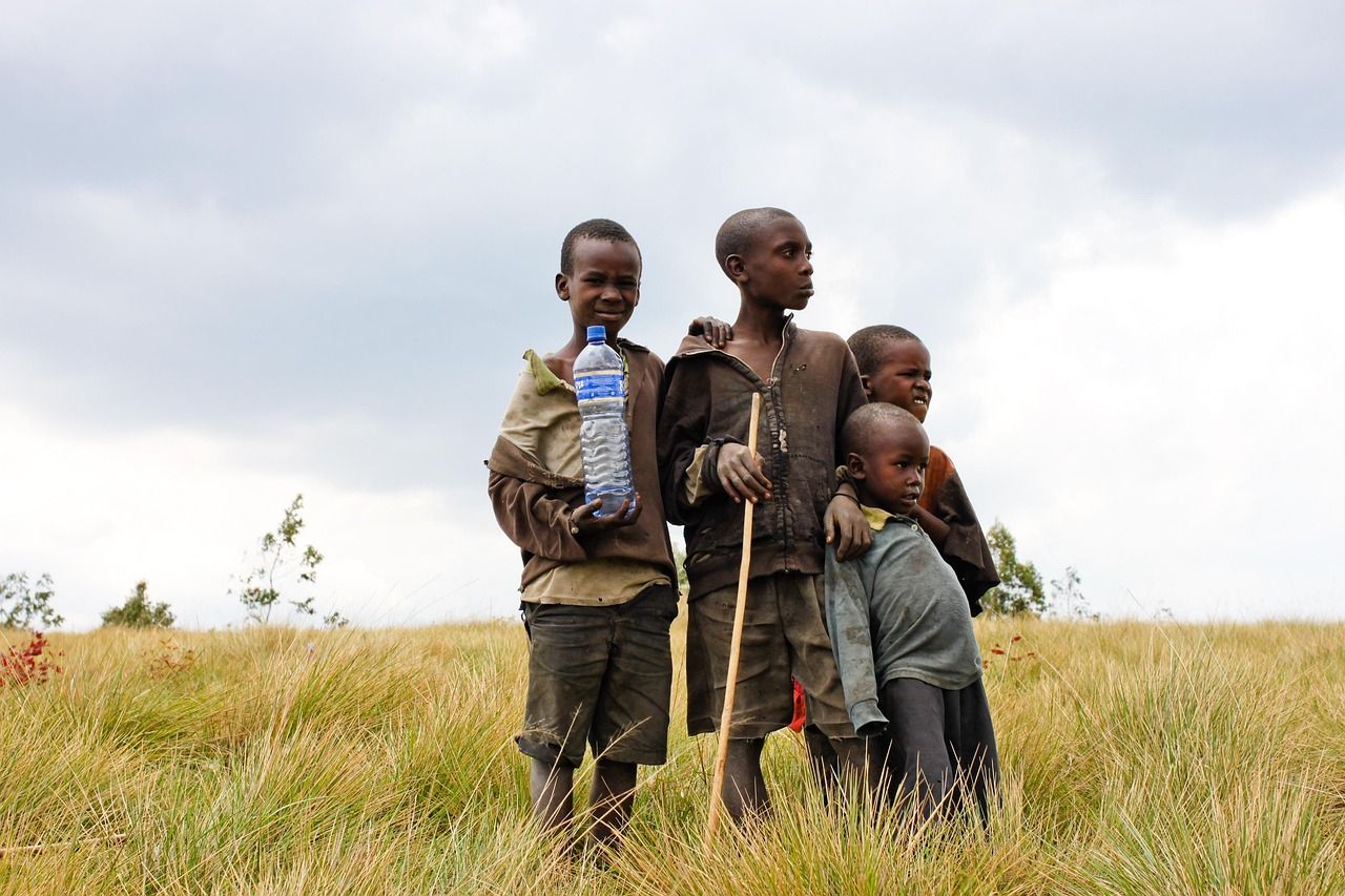 Four children standing in tall grass, one holding a plastic water bottle