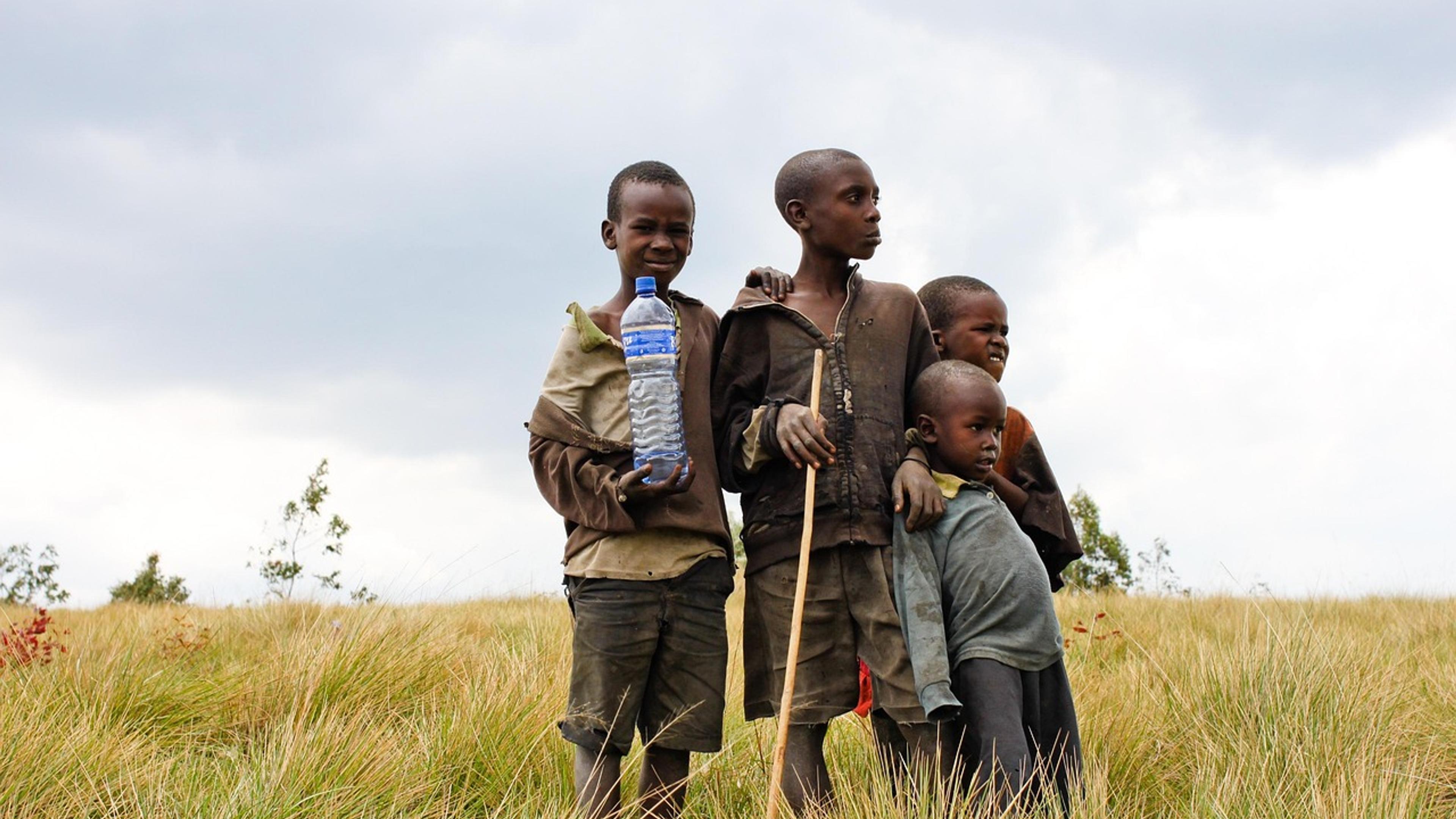 Four children standing in tall grass, one holding a plastic water bottle