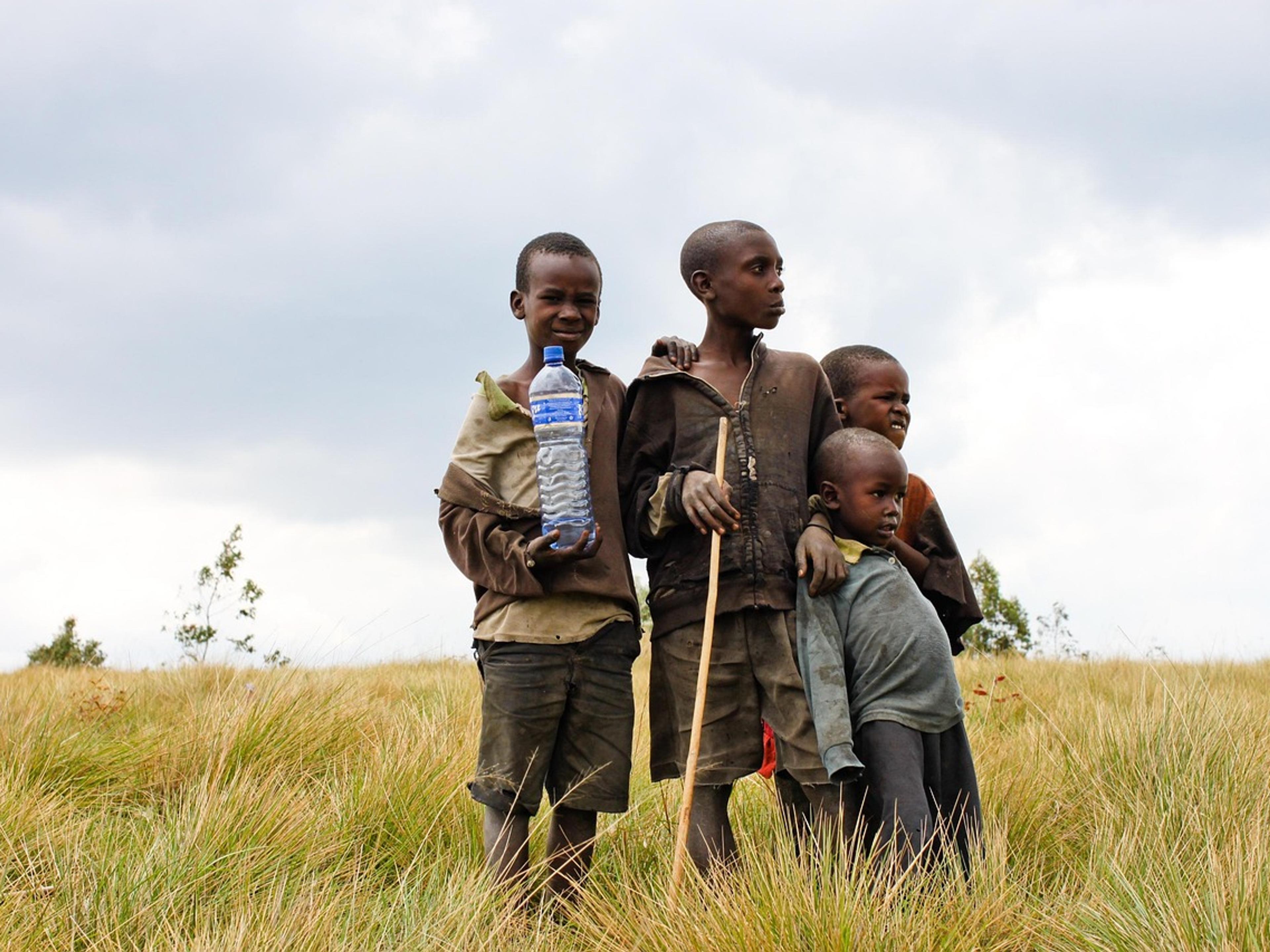 Four children standing in tall grass, one holding a plastic water bottle