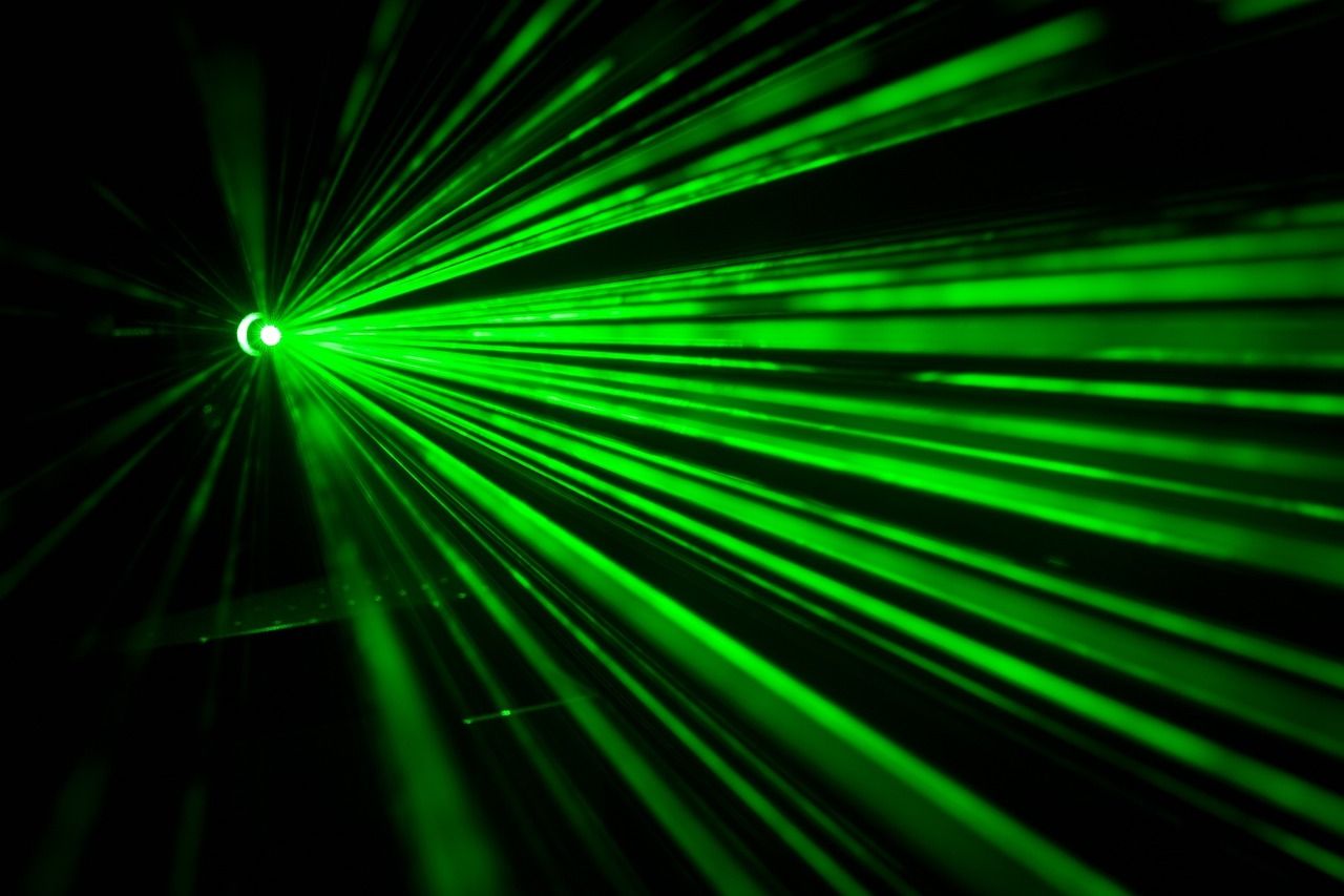 Green laser beams fanning out through haze against a dark background
