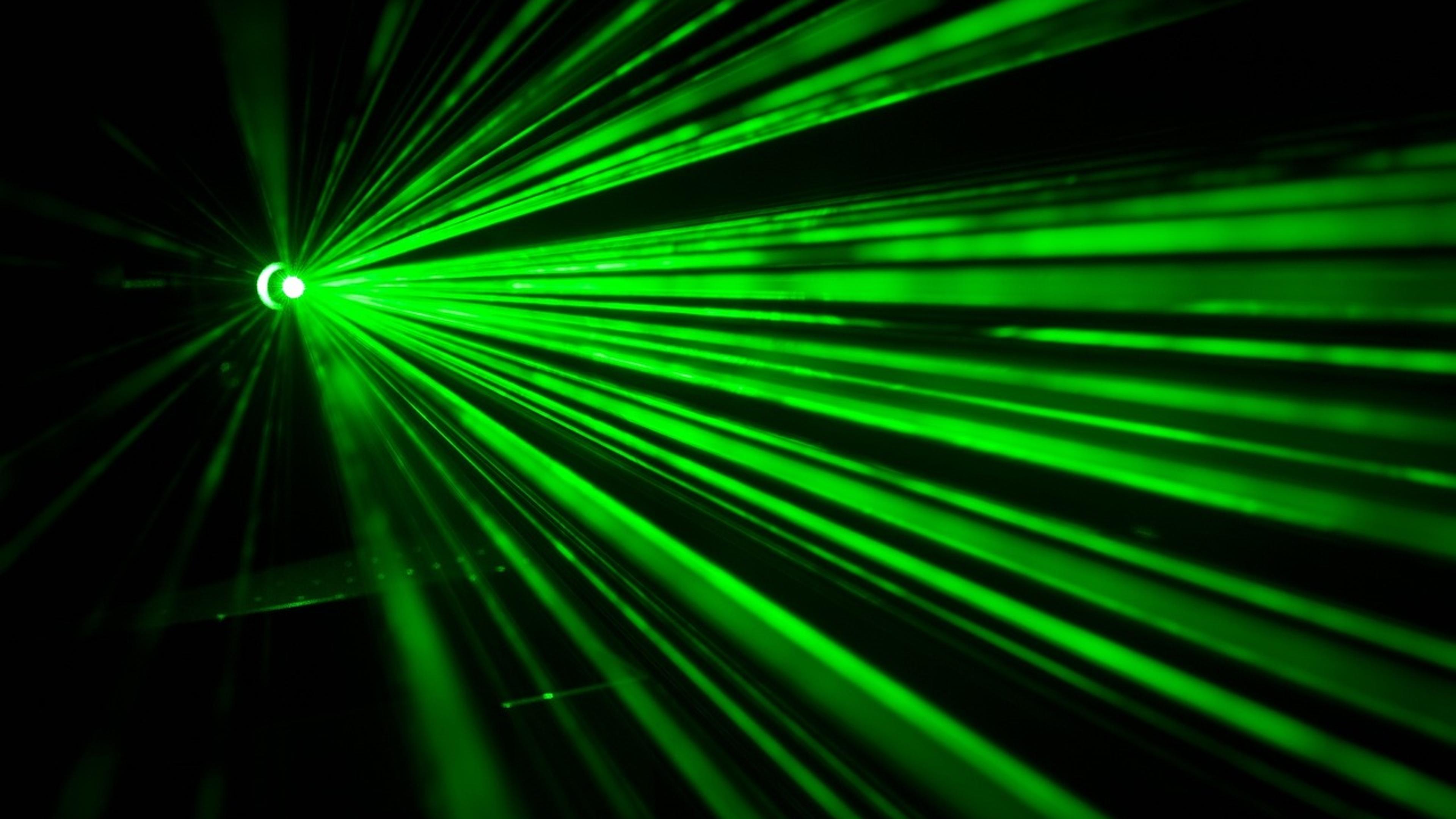 Green laser beams fanning out through haze against a dark background