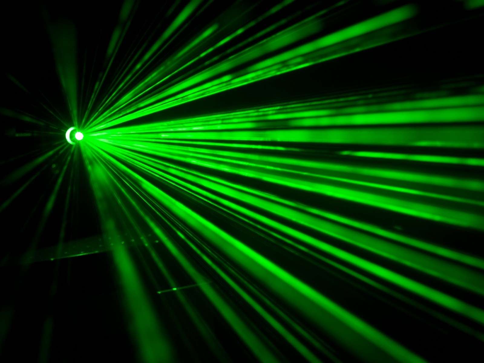 Green laser beams fanning out through haze against a dark background