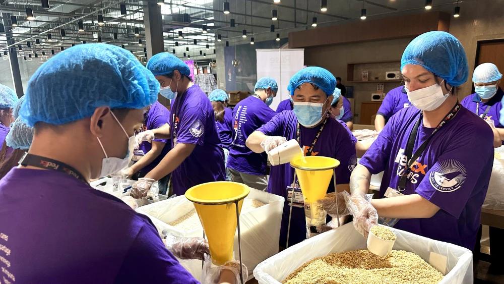 Volunteers in matching sweaters packing food donations into cardboard boxes together, working as a team indoors