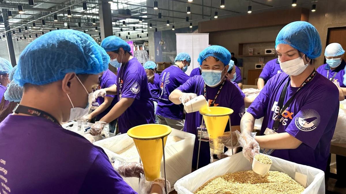 Volunteers in matching sweaters packing food donations into cardboard boxes together, working as a team indoors