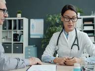 A doctor consulting with an older male patient at a desk in a modern medical office.
