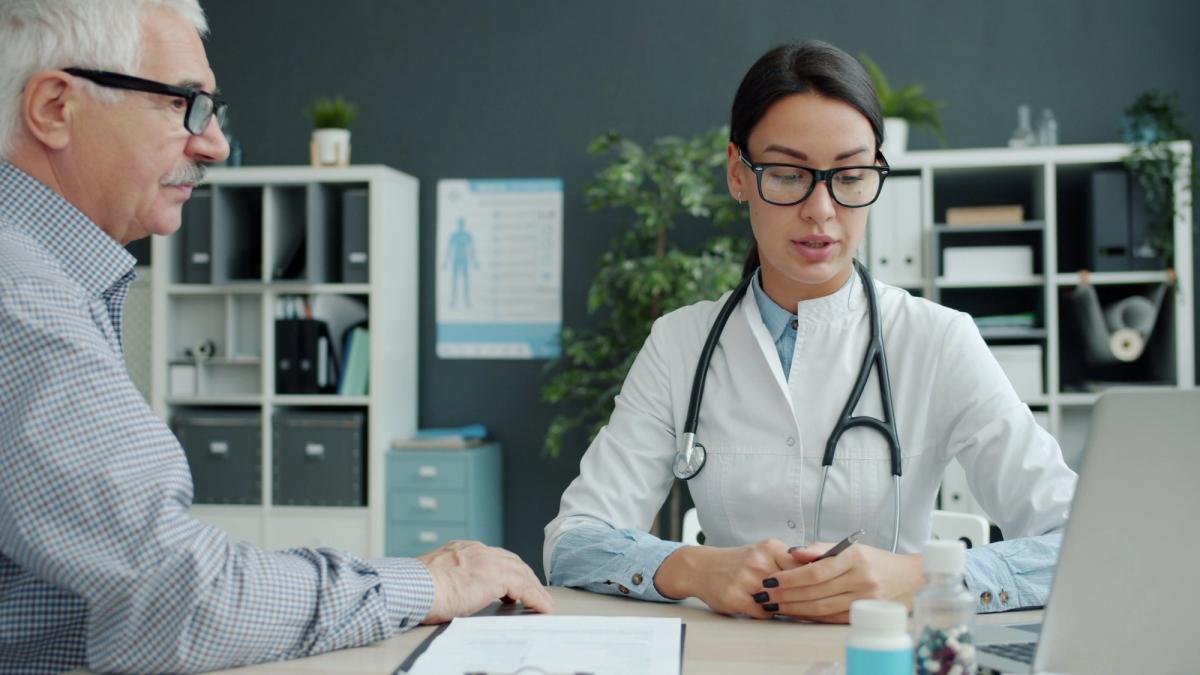 A doctor consulting with an older male patient at a desk in a modern medical office.