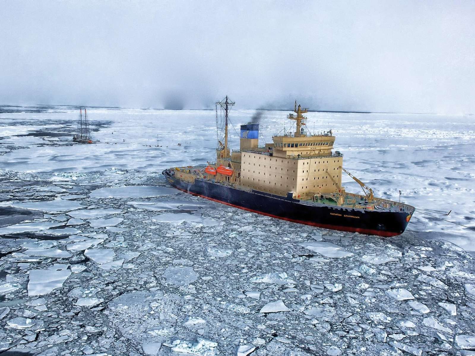 An icebreaker ship pushing through broken sea ice, with a sailing ship in the distance