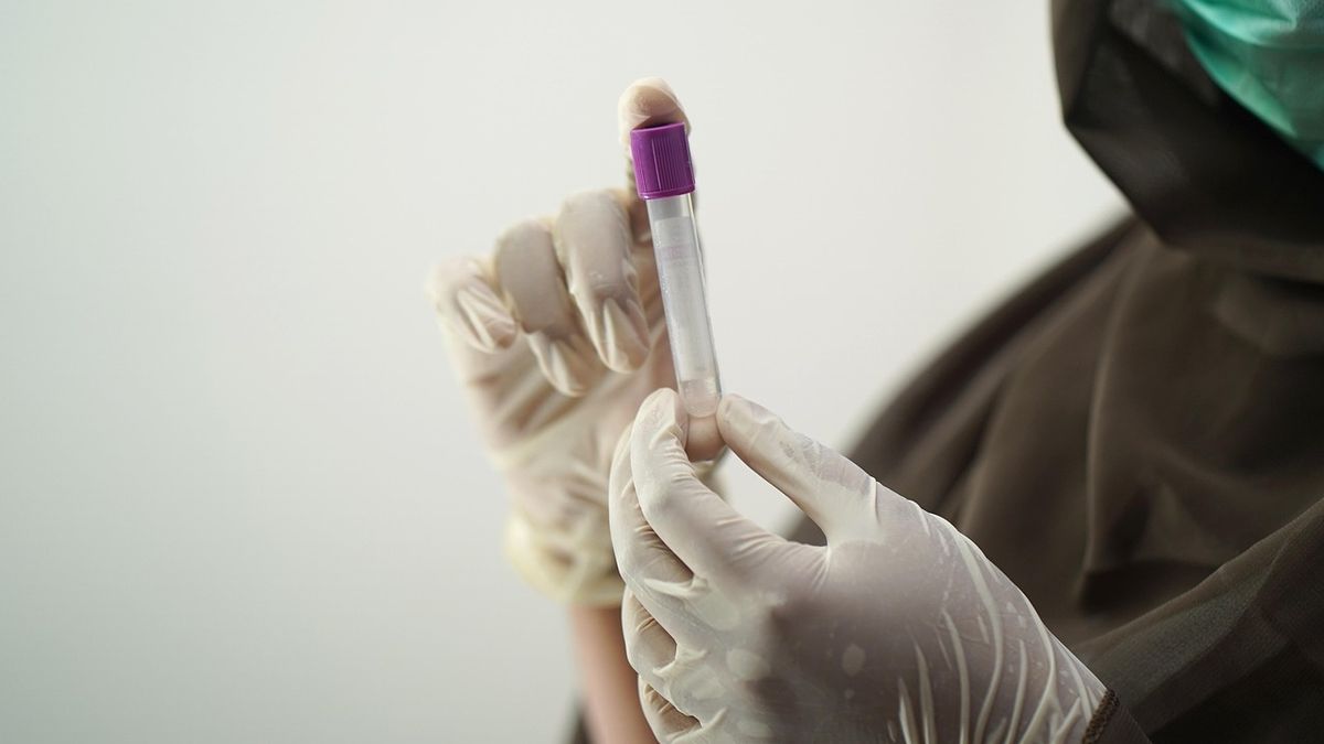 Lab technician in surgical gloves handling a blood sample tube