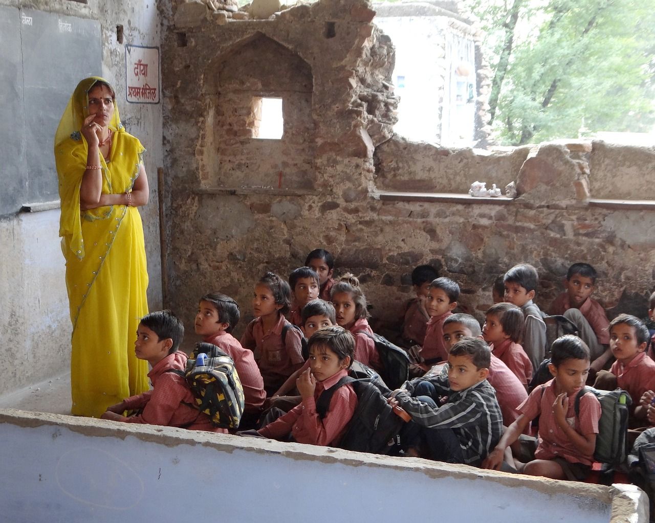 A teacher in a yellow sari in front of a crowded classroom of children in India
