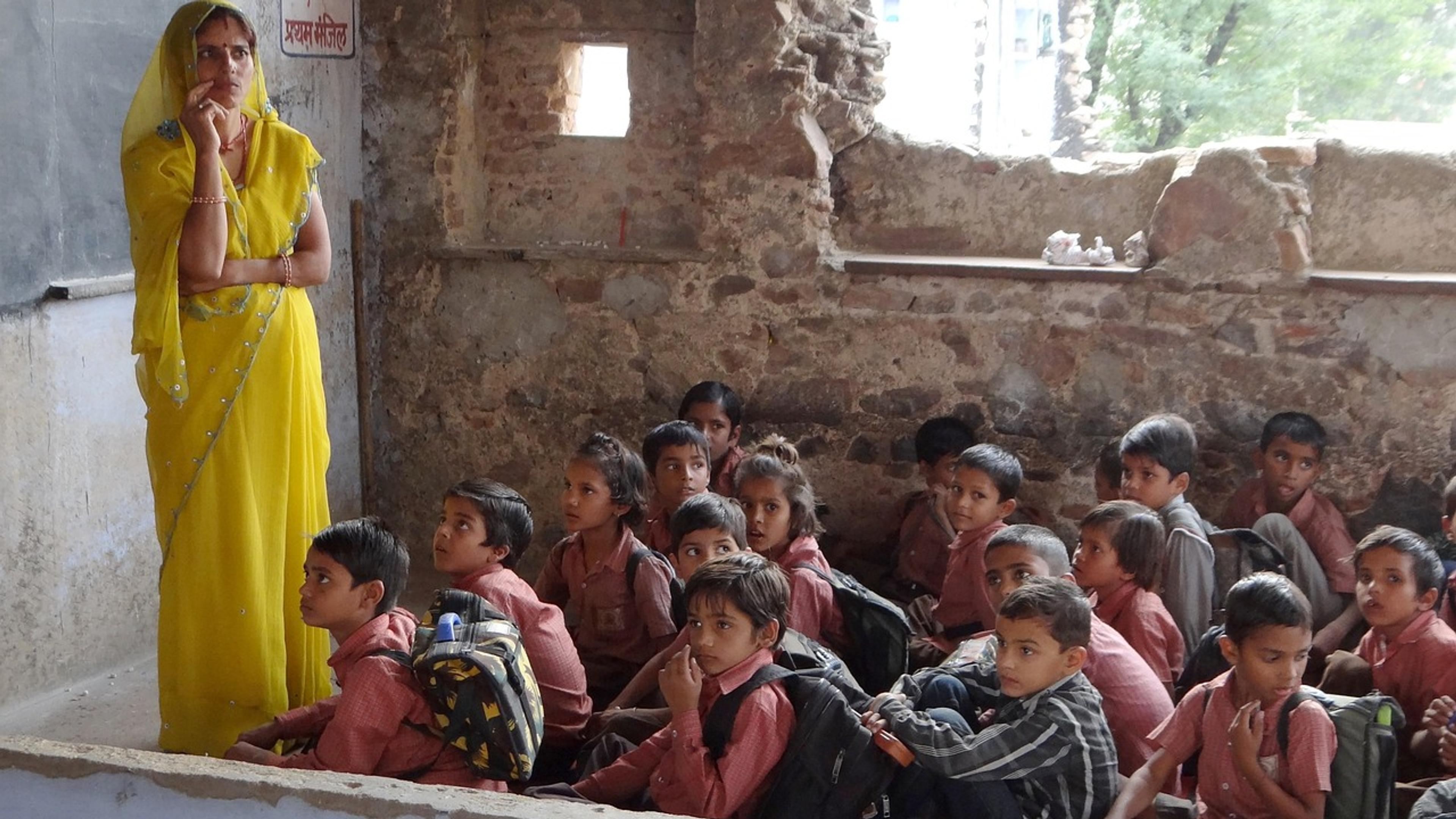 A teacher in a yellow sari in front of a crowded classroom of children in India