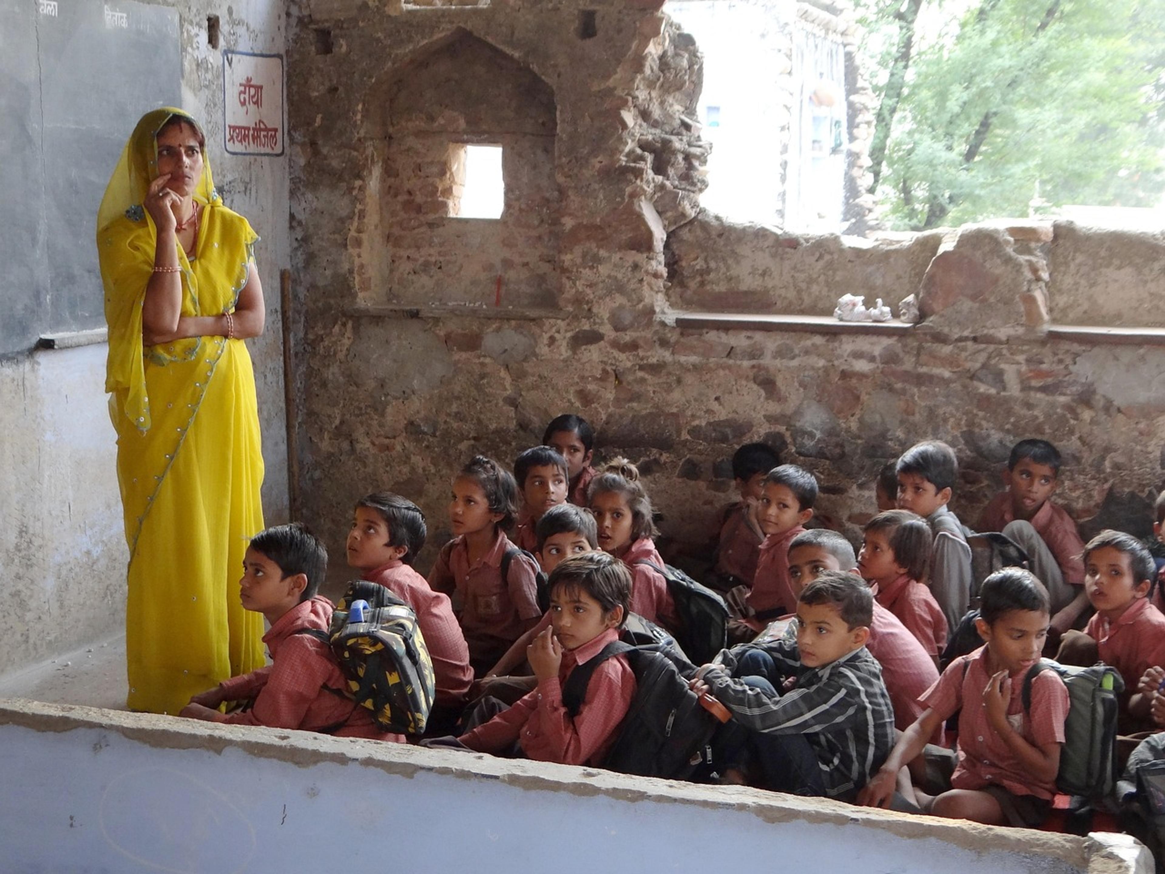 A teacher in a yellow sari in front of a crowded classroom of children in India