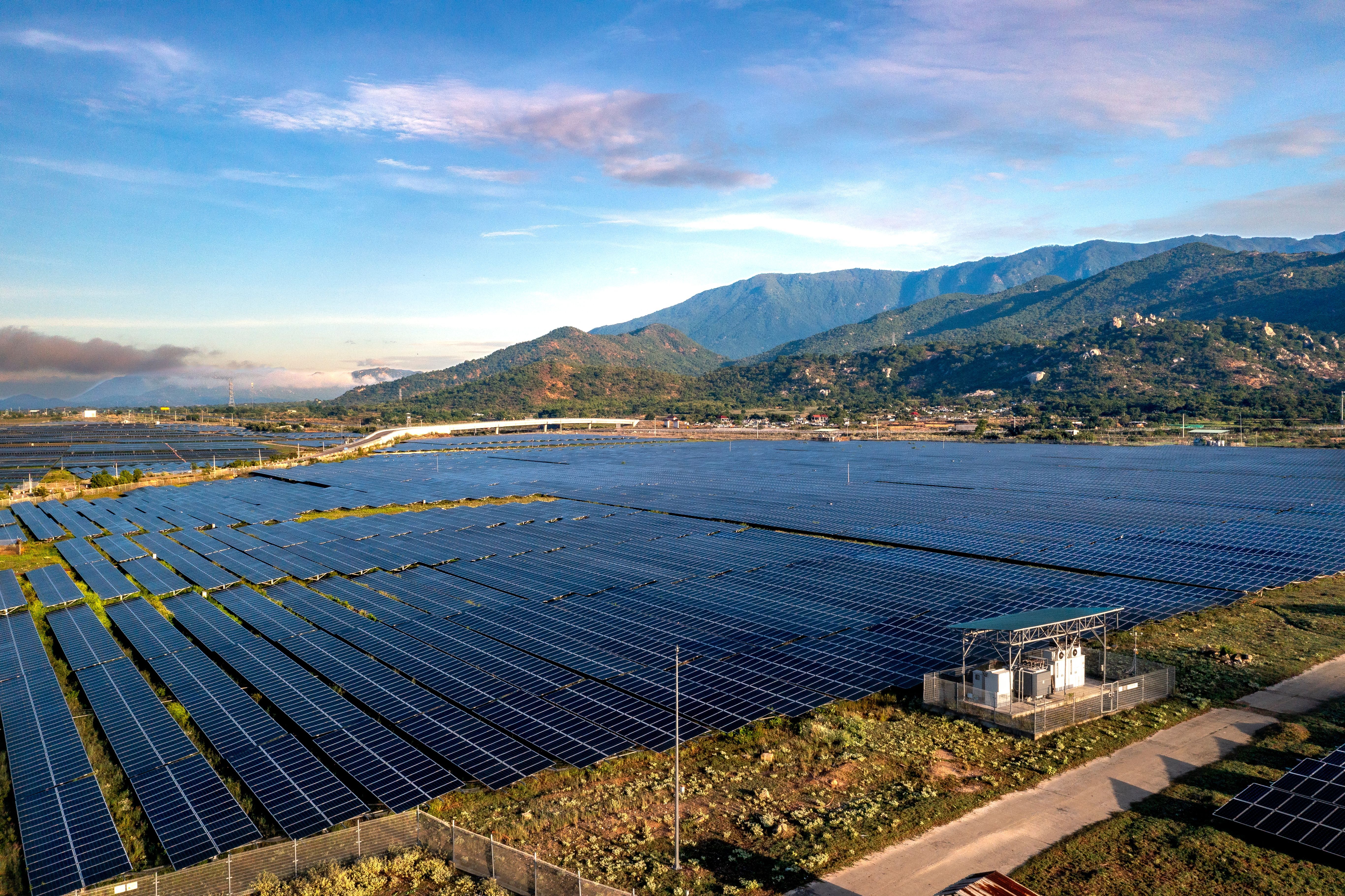 Aerial view of a large solar panel farm set against a mountainous backdrop, representative of the mountainous terrain where Bhutan's Sephu Solar Power Project is located.