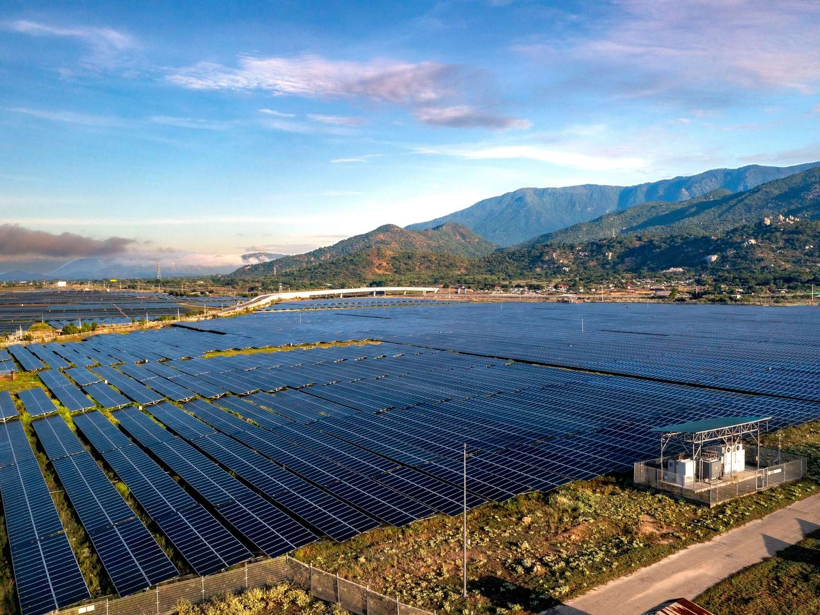 Aerial view of a large solar panel farm set against a mountainous backdrop, representative of the mountainous terrain where Bhutan's Sephu Solar Power Project is located.