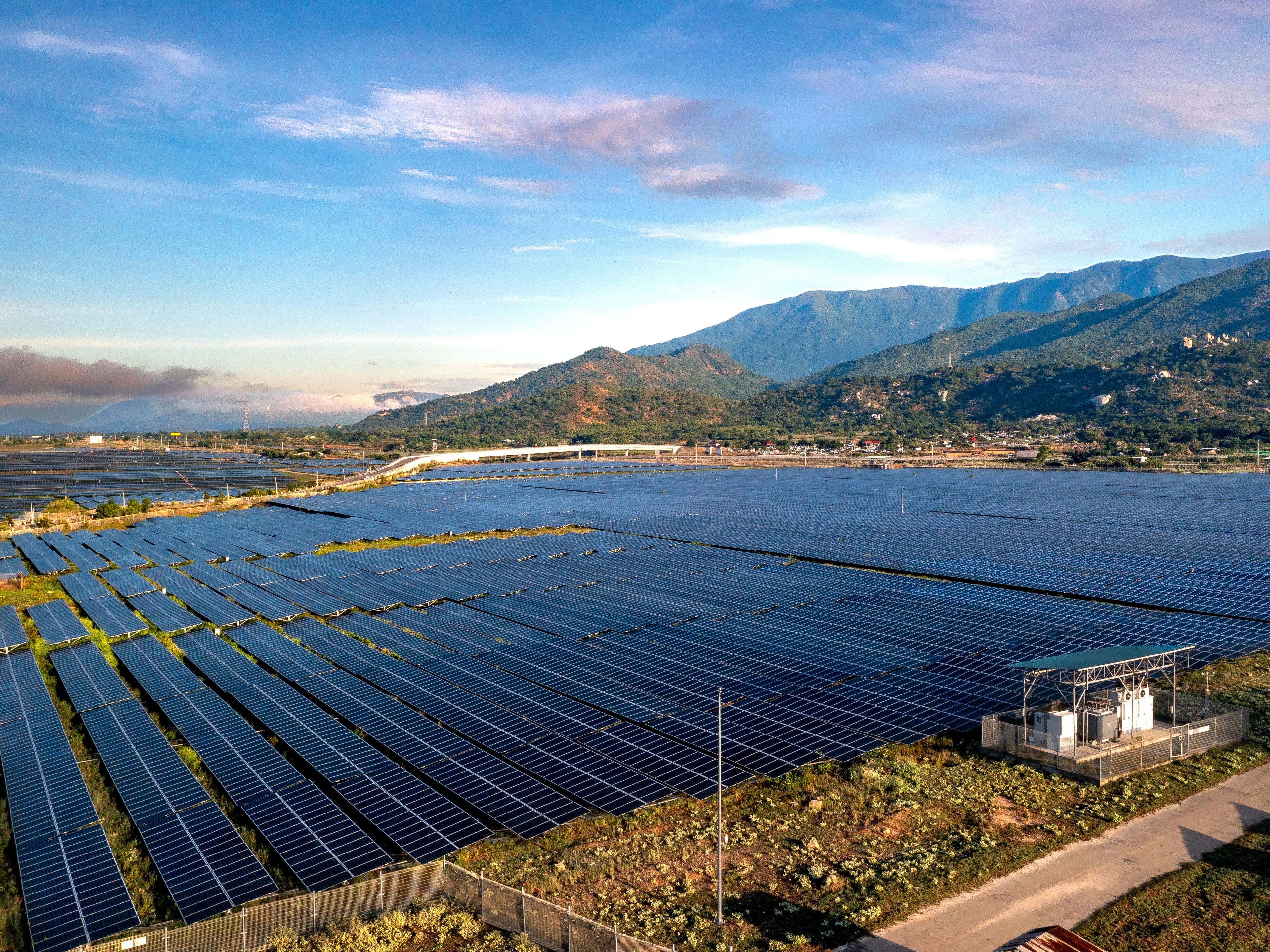 Aerial view of a large solar panel farm set against a mountainous backdrop, representative of the mountainous terrain where Bhutan's Sephu Solar Power Project is located.