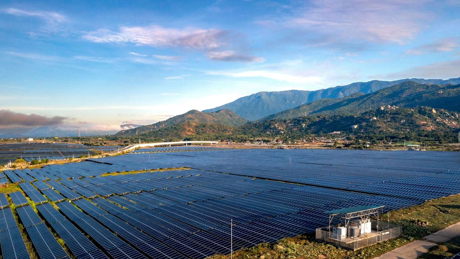 Aerial view of a large solar panel farm set against a mountainous backdrop, representative of the mountainous terrain where Bhutan's Sephu Solar Power Project is located.