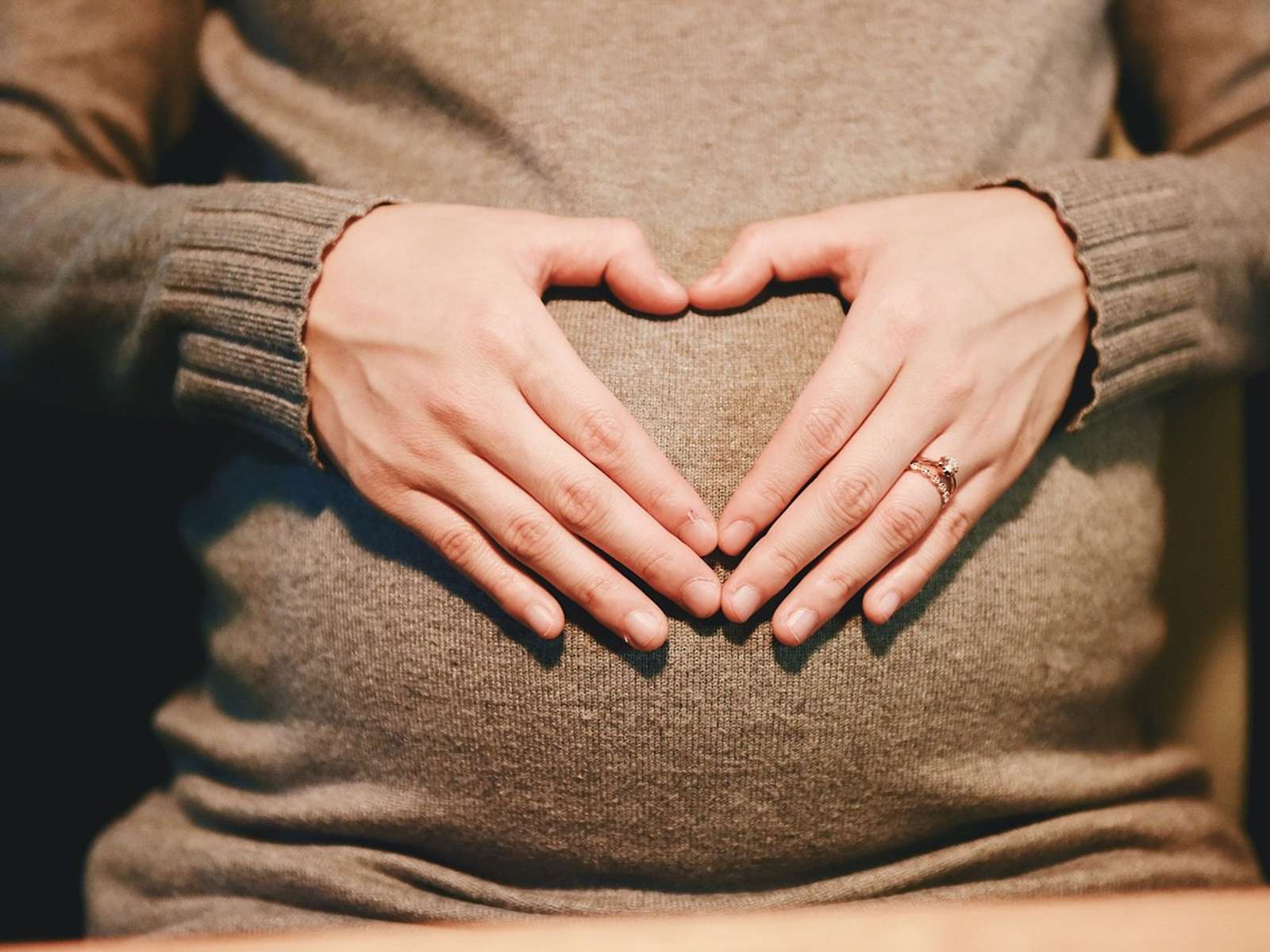 A pregnant woman in a knitted sweater forming a heart shape with her hands over her belly