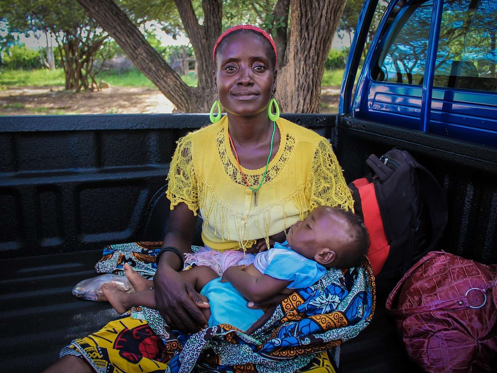 A smiling African woman in a yellow top holding a sleeping baby on her lap