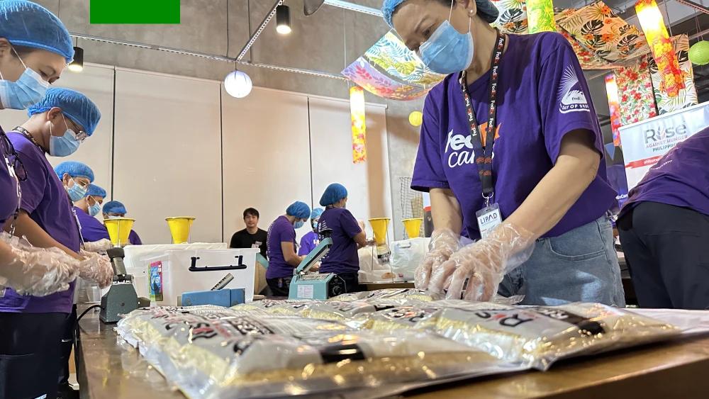 Volunteers in matching sweaters packing food donations into cardboard boxes together, working as a team indoors