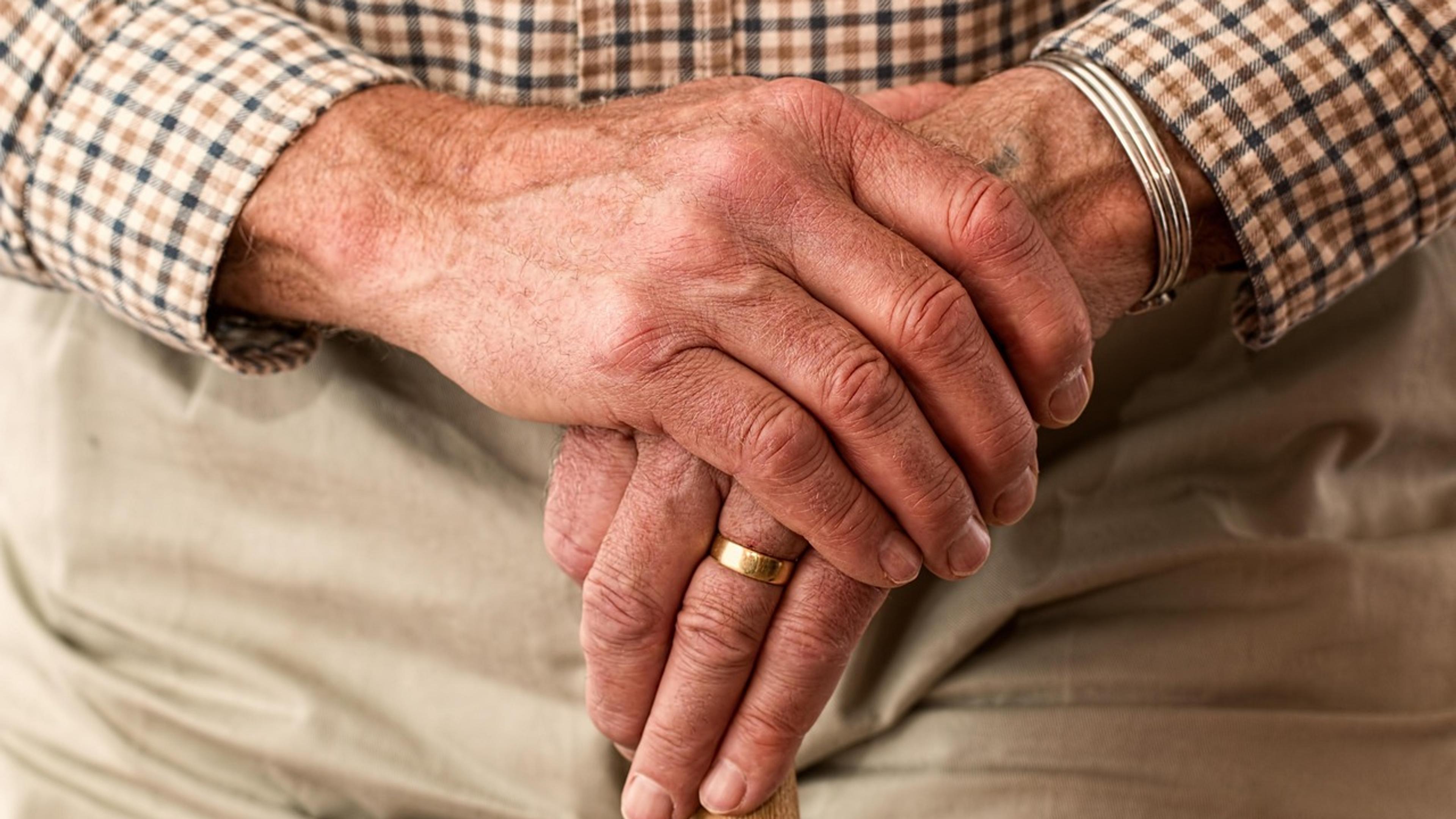 An older man's hands resting on a wooden walking stick