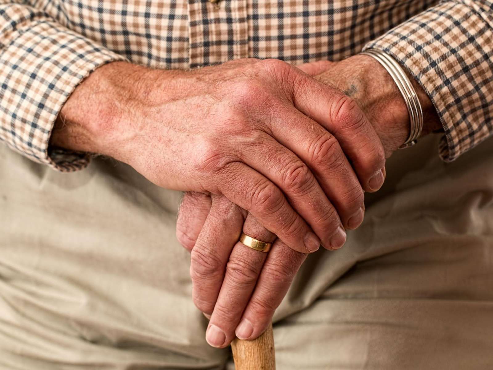 An older man's hands resting on a wooden walking stick