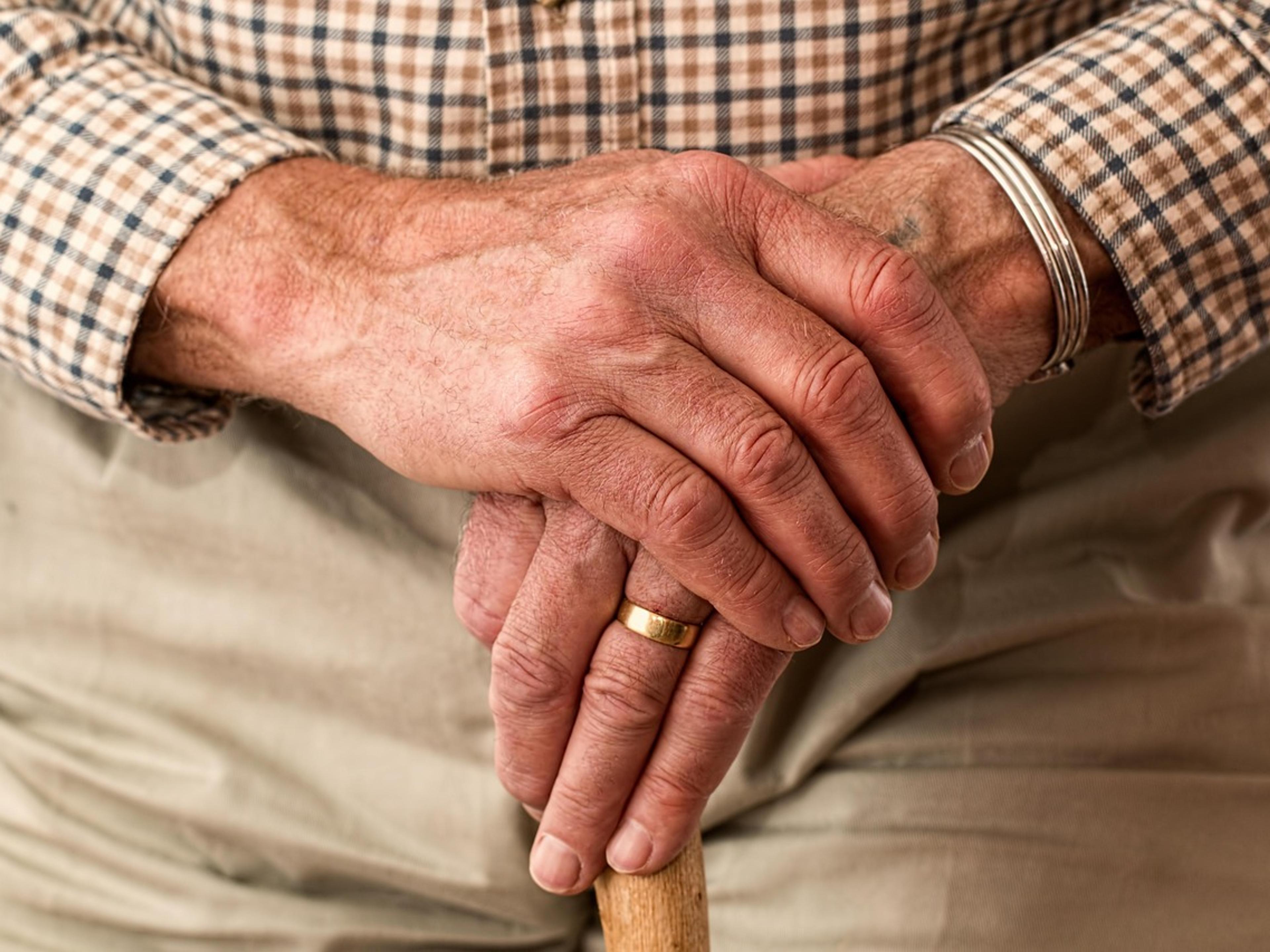 An older man's hands resting on a wooden walking stick