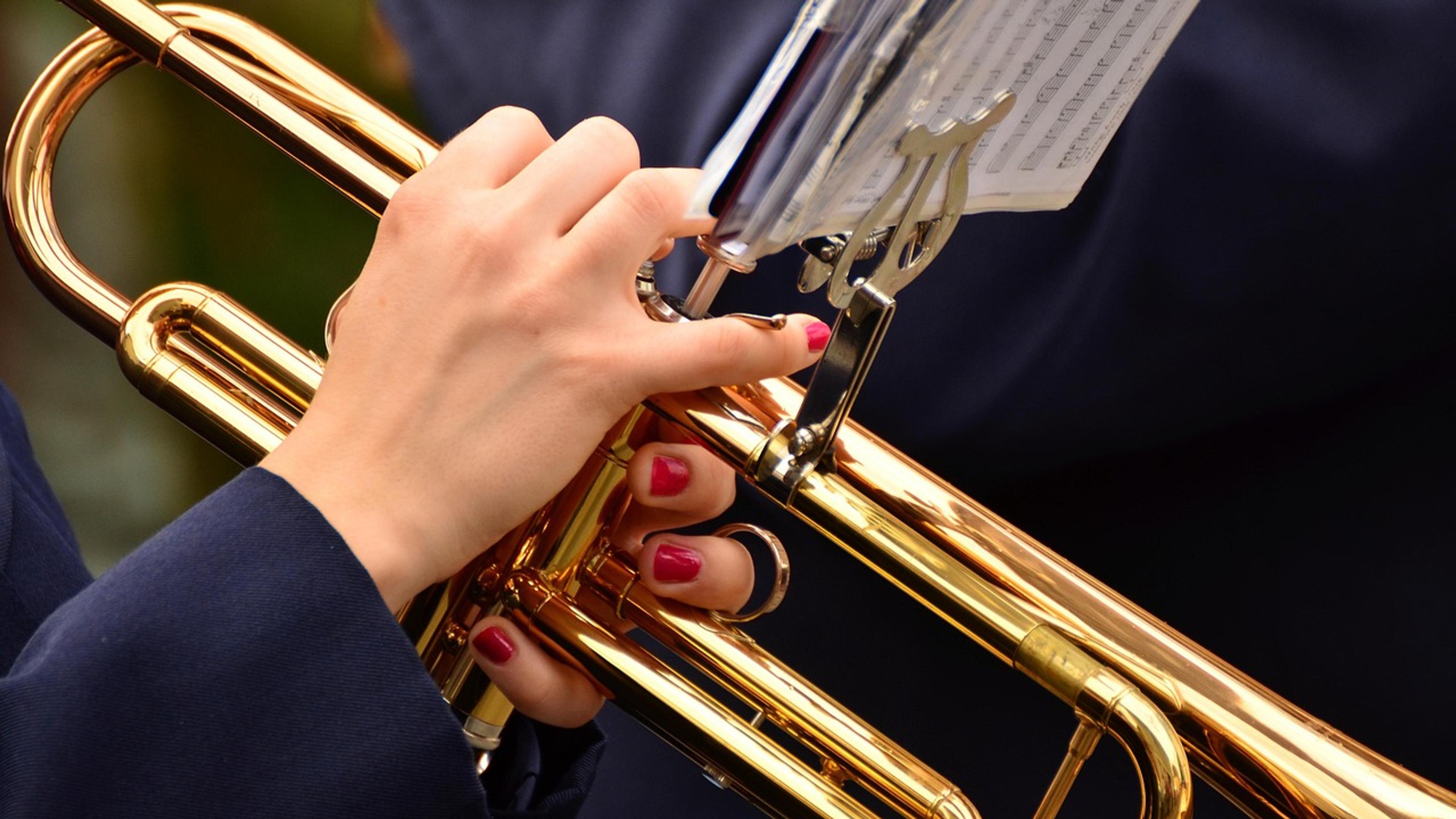 Close-up of hands holding a brass trumpet in front of sheet music