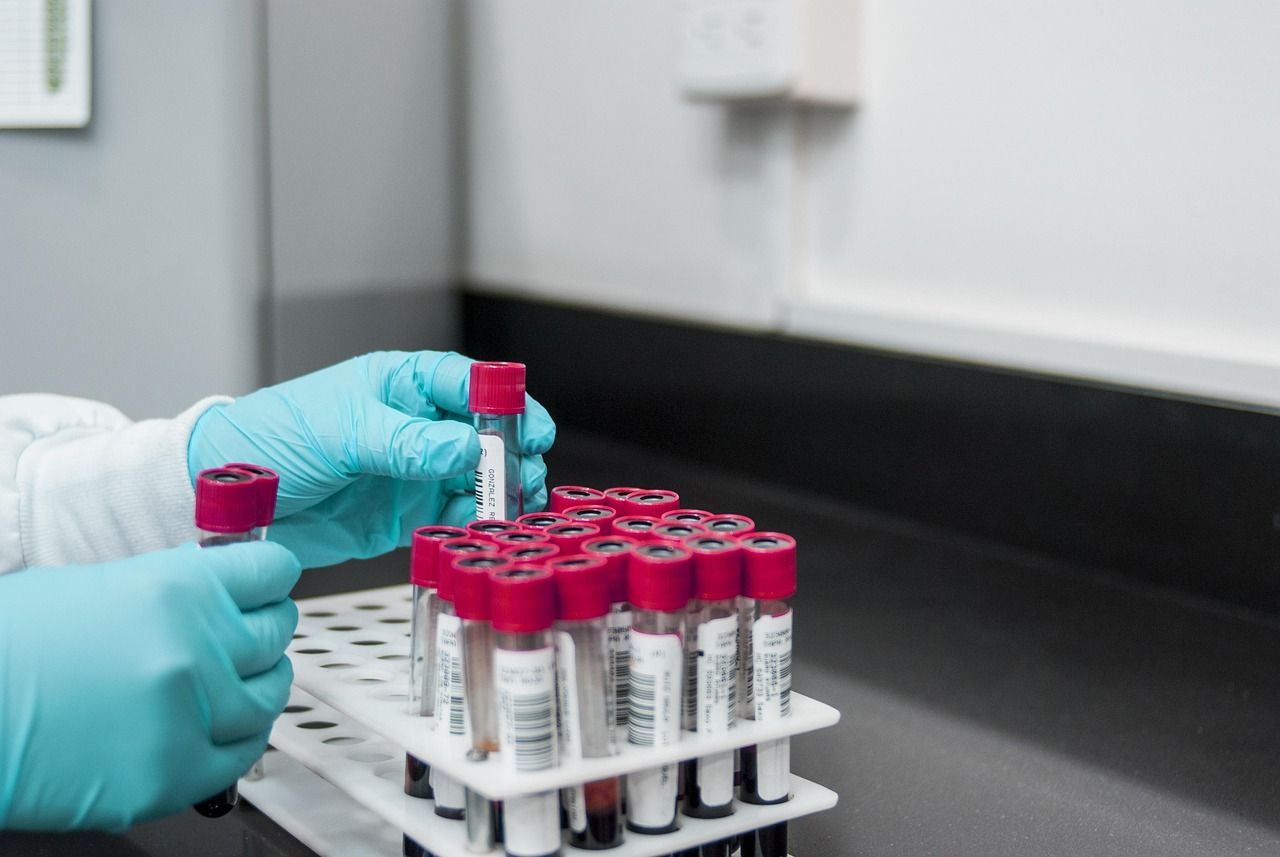 A lab technician in blue gloves handling a rack of sample tubes