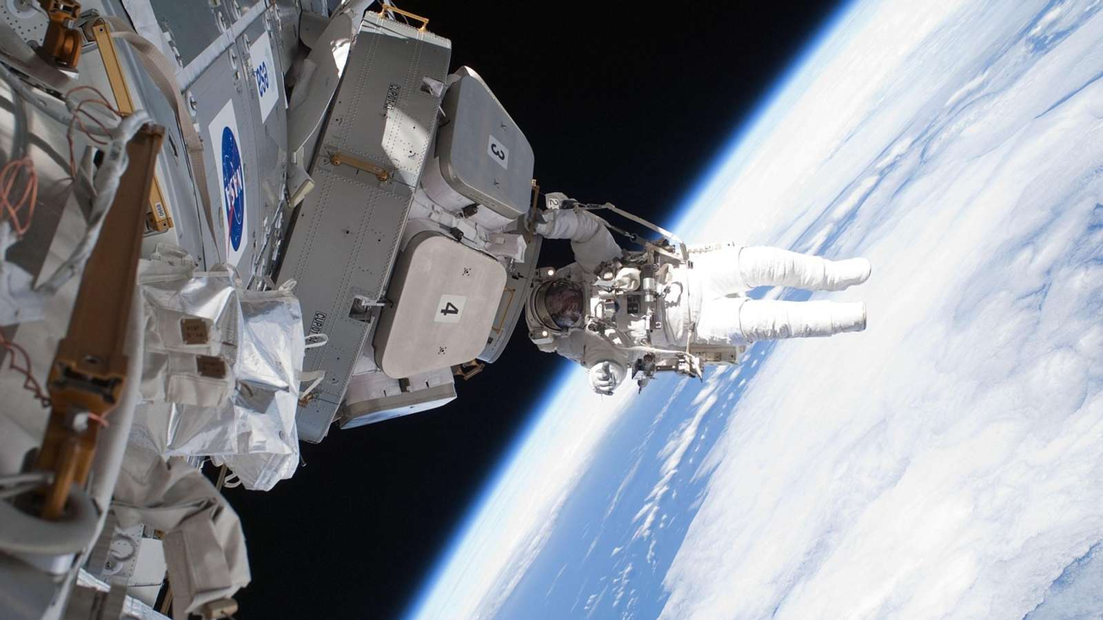 Archive NASA photo of an astronaut on a spacewalk outside the International Space Station, with Earth's clouds below