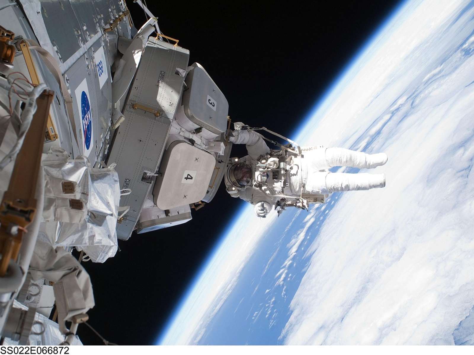 Archive NASA photo of an astronaut on a spacewalk outside the International Space Station, with Earth's clouds below