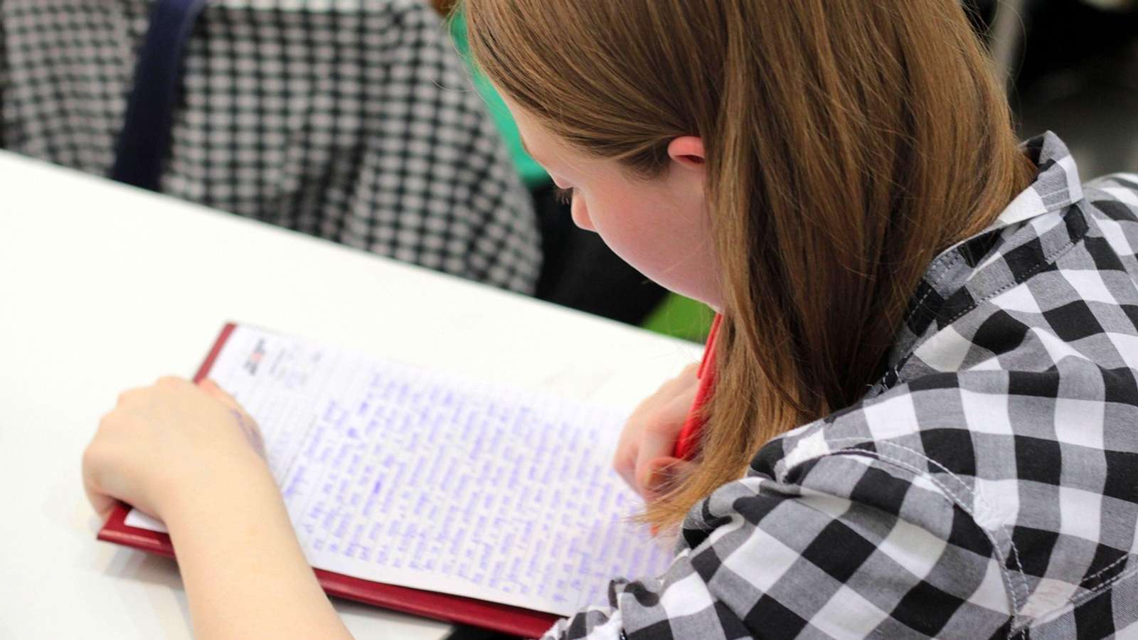 A student's hand writing in a notebook with a pen at a school desk