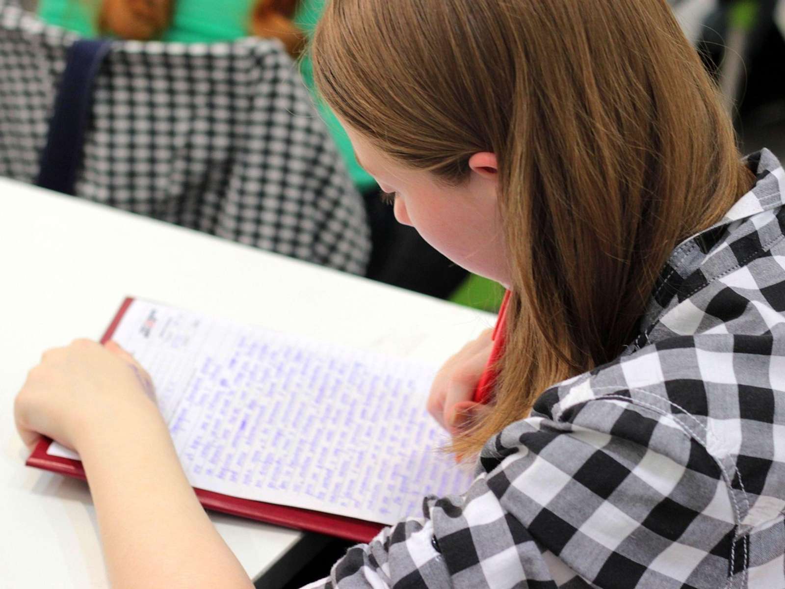 A student's hand writing in a notebook with a pen at a school desk