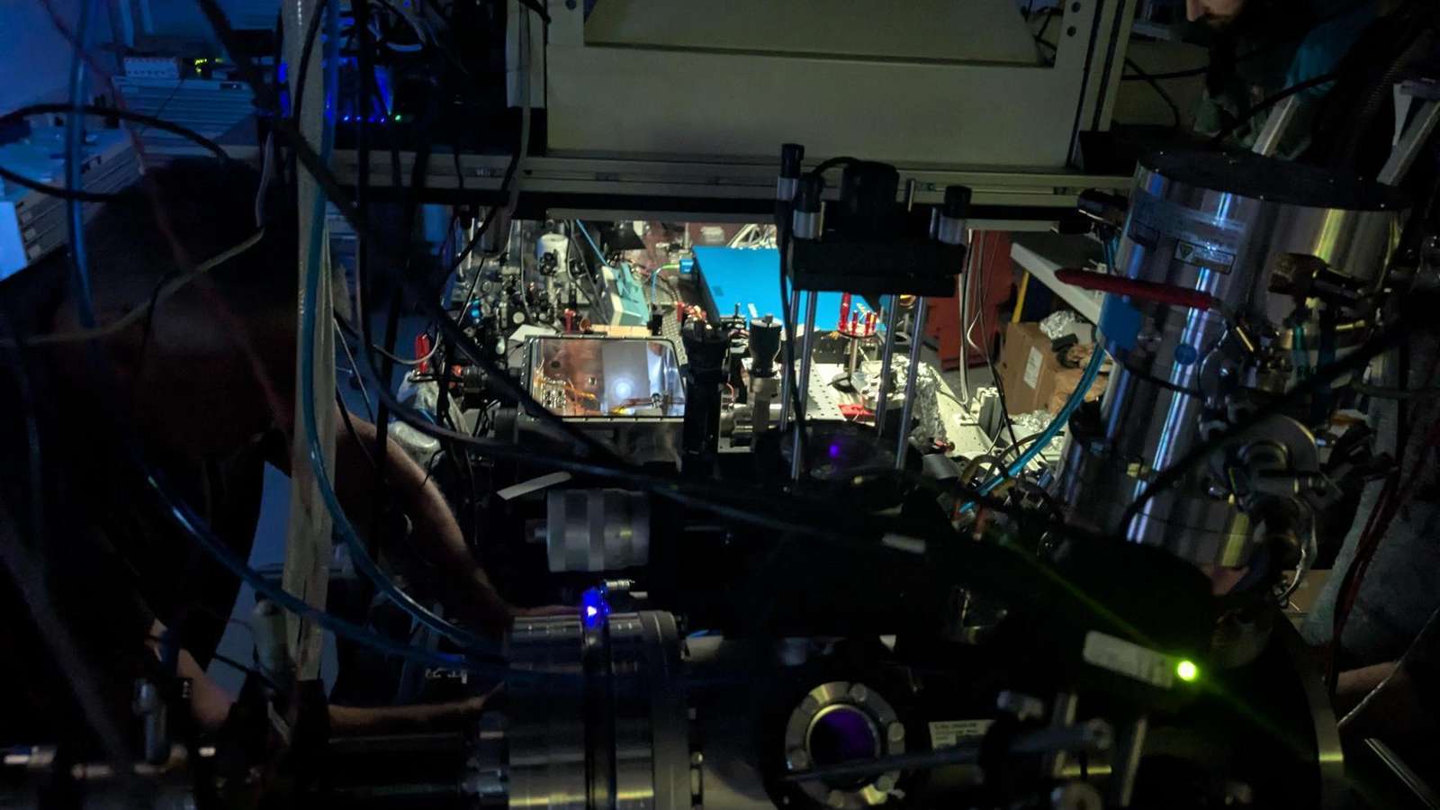 Researchers working at a darkened laser laboratory with vacuum chambers, cables and optical equipment at TU Wien