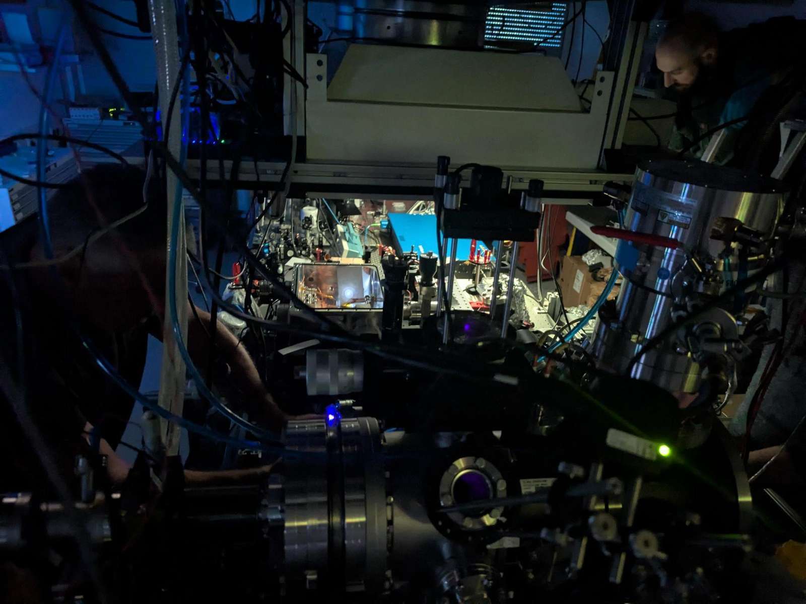 Researchers working at a darkened laser laboratory with vacuum chambers, cables and optical equipment at TU Wien