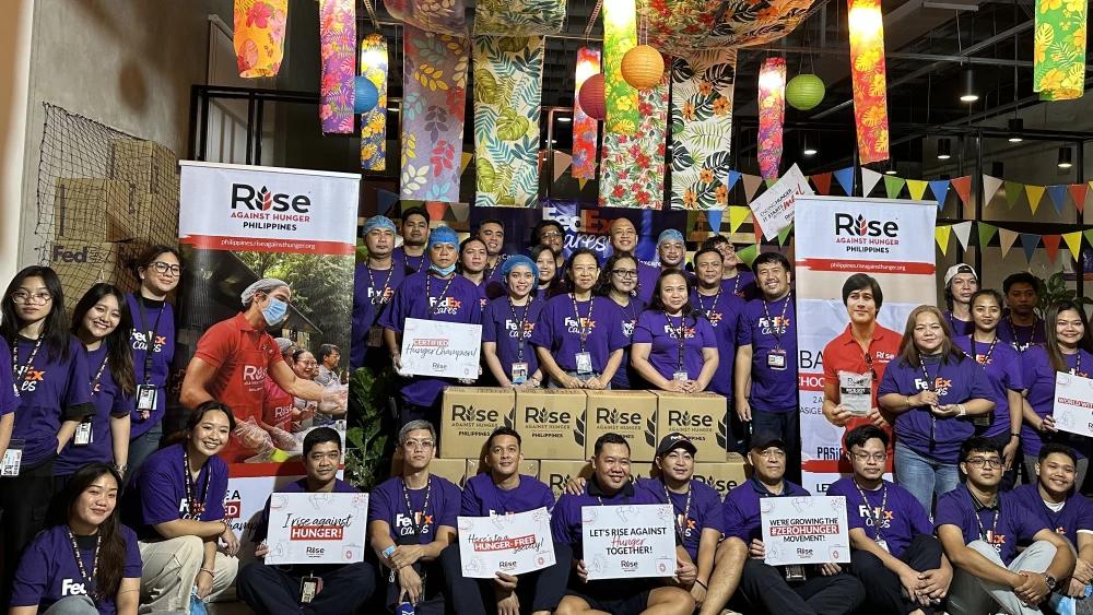 Group photo of FedEx volunteers in purple shirts with Rise Against Hunger Philippines banners, boxed meal kits and hand-written signs