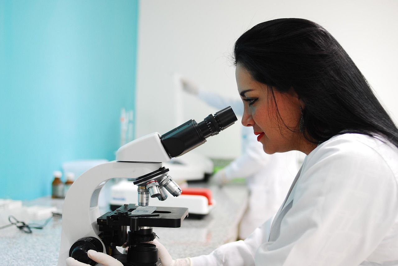A scientist in a white lab coat looking into a microscope in a bright laboratory