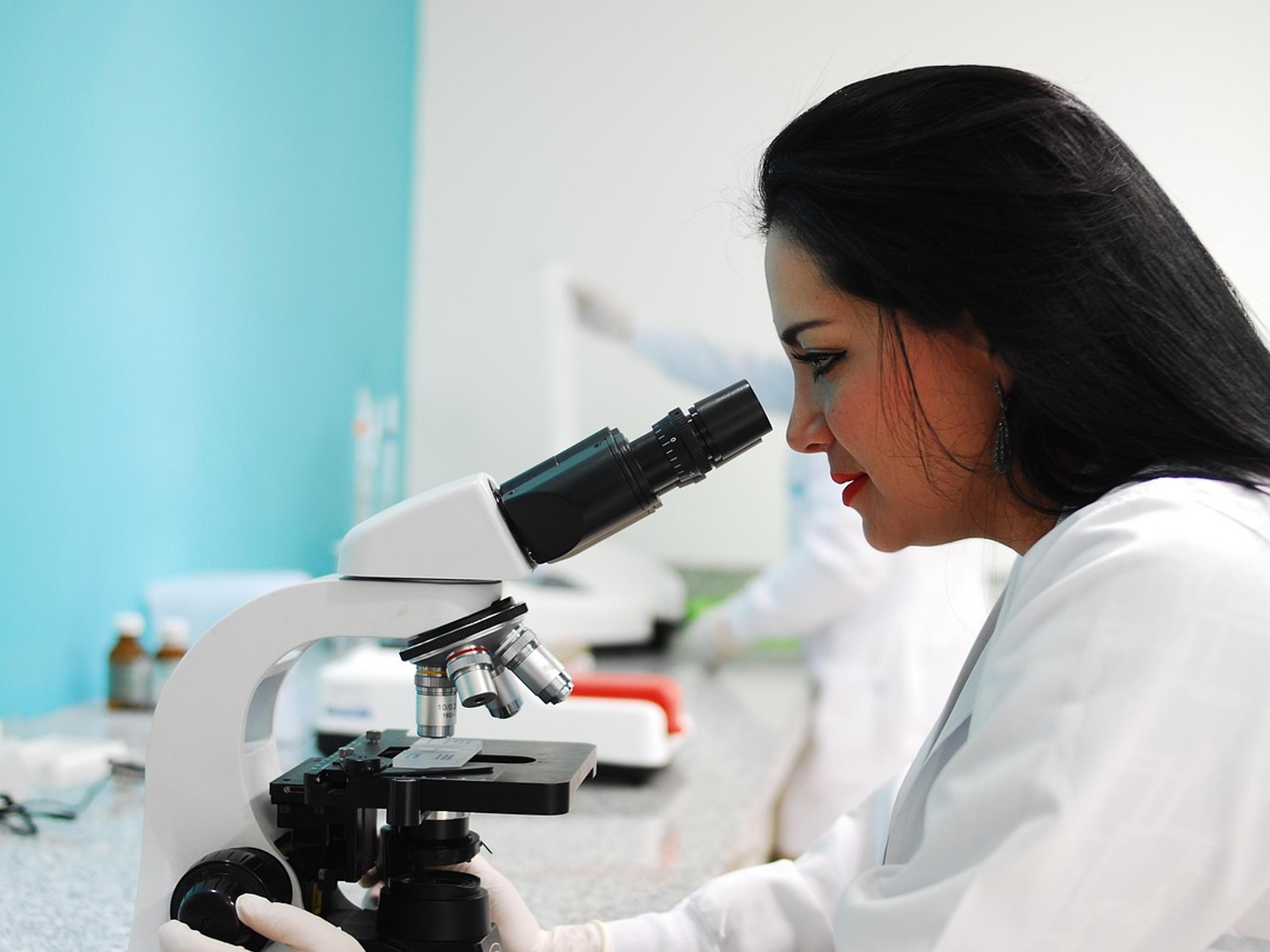 A scientist in a white lab coat looking into a microscope in a bright laboratory